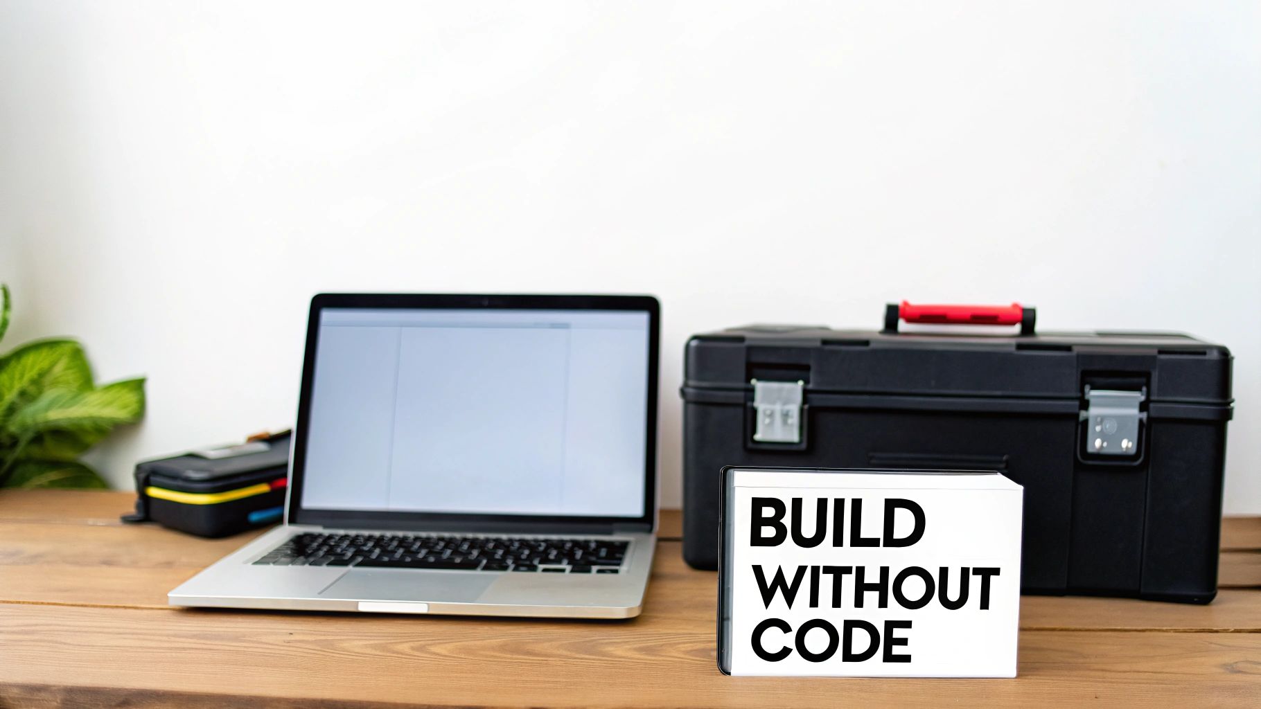 A no-code development workspace featuring a laptop, black toolbox, and a "BUILD WITHOUT CODE" sign.