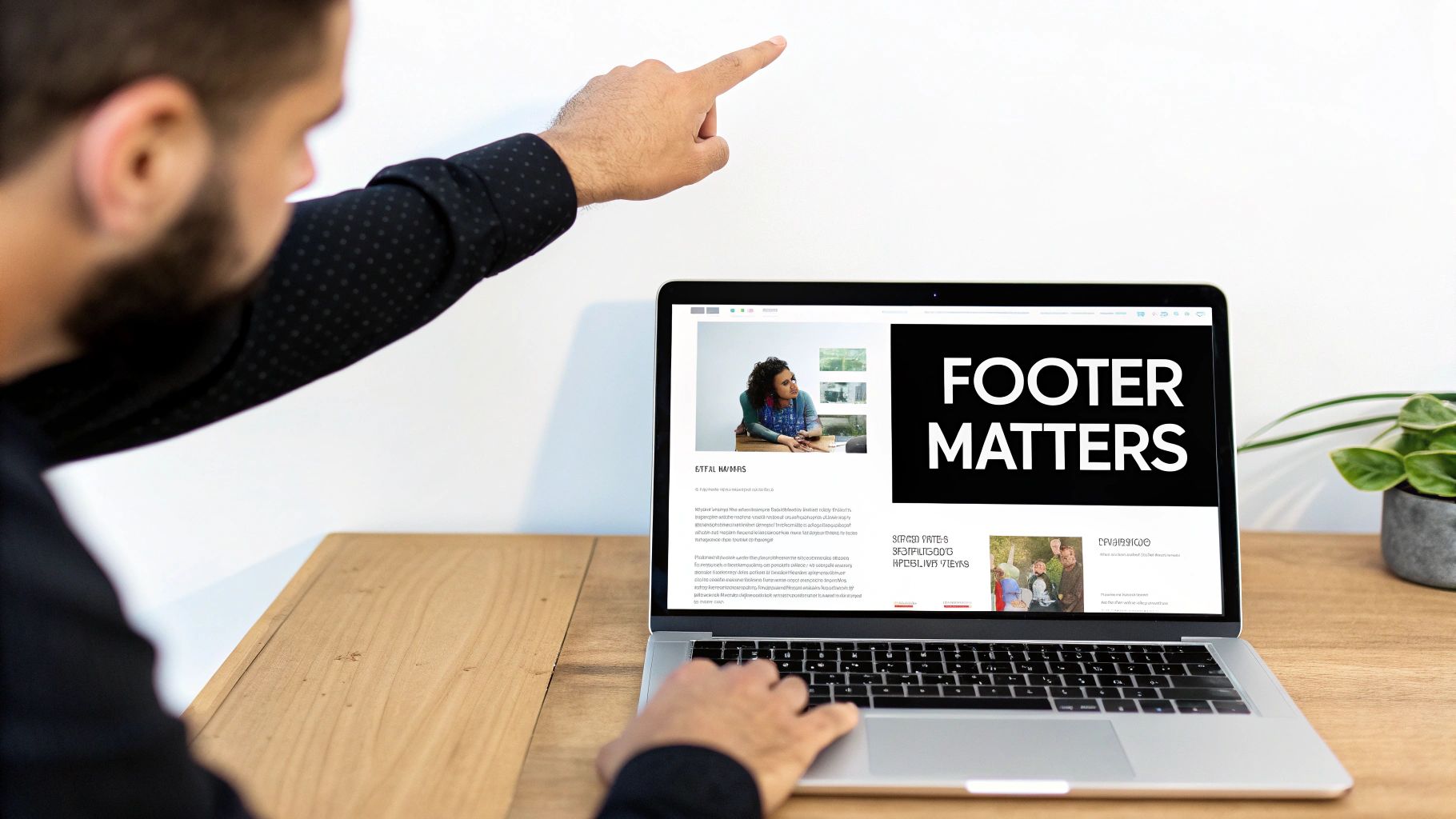 A man points at a laptop screen displaying a webpage with the text 'FOOTER MATTERS' on a wooden desk.