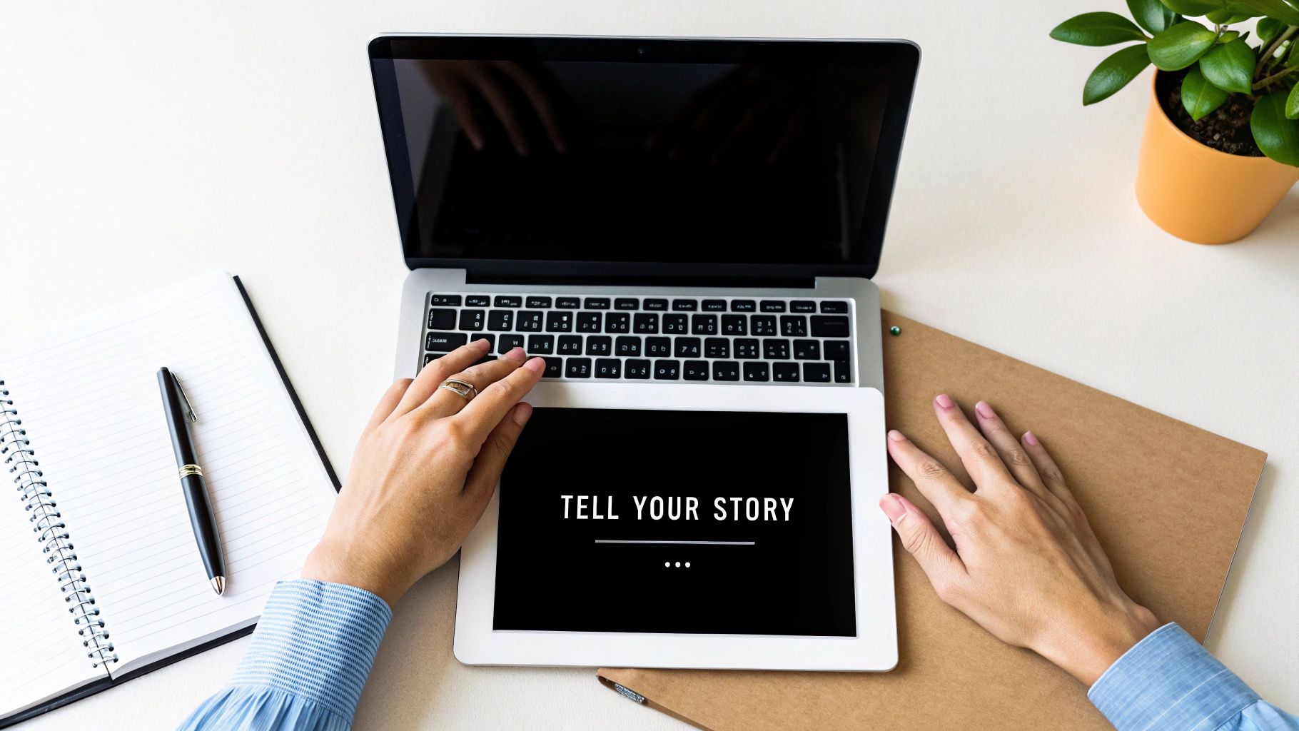 A person writing in a notebook at a sunlit wooden desk, with a laptop and a cup of tea nearby.