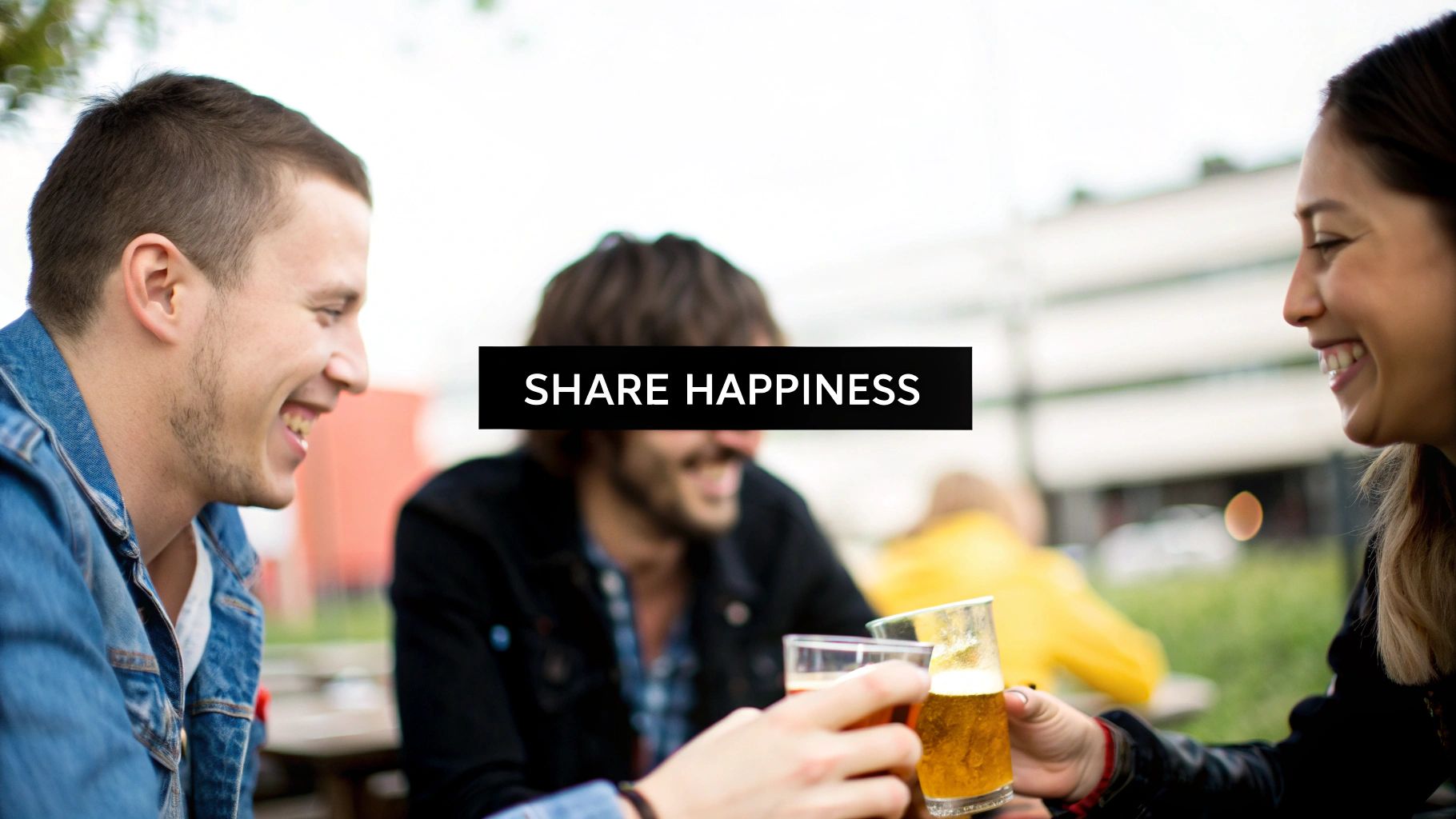 Three happy friends laughing and toasting with beer glasses outdoors, sharing happiness.