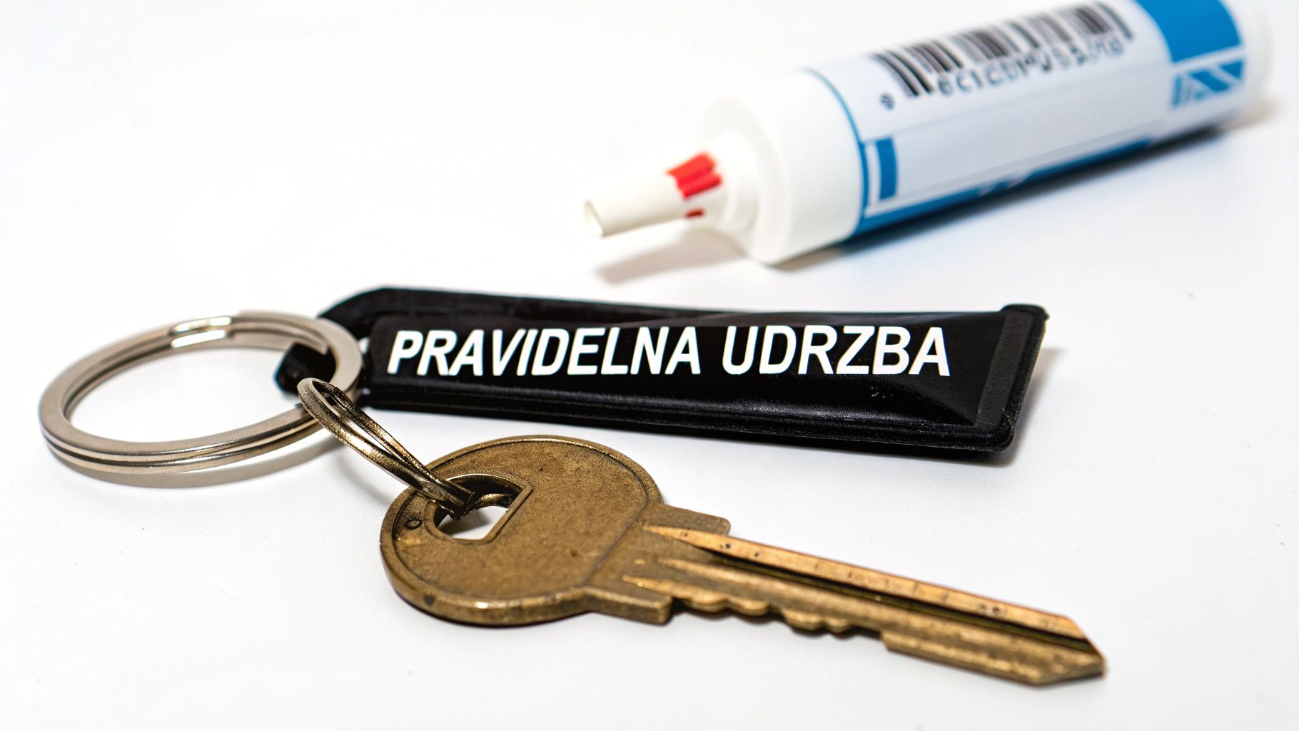 Klíče s přívěskem na klíče s nápisem 'Pravidelná údržba' a bílá tuba na bílém pozadí.