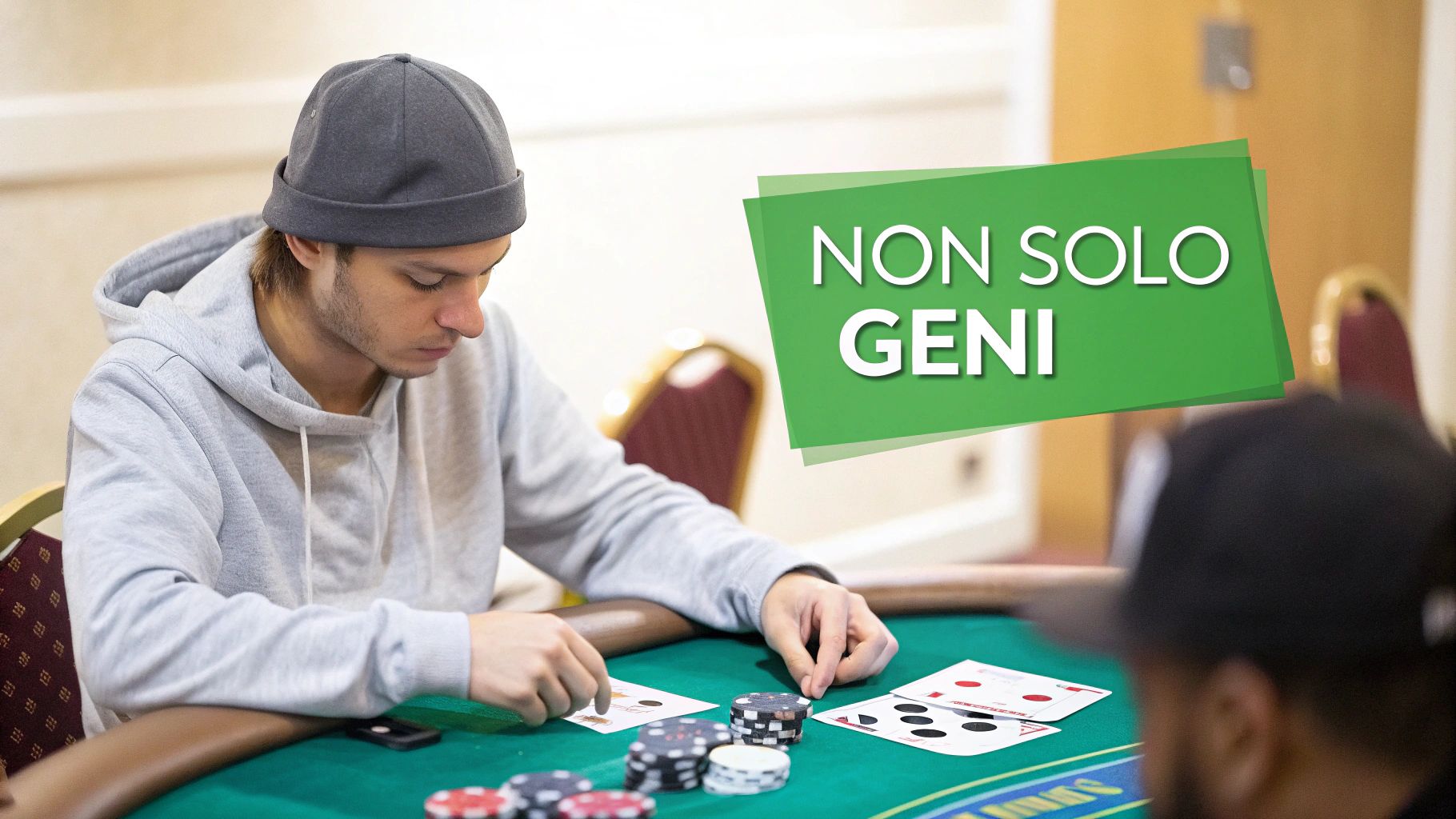 Un giovane uomo con un cappello e una felpa grigia gioca a poker a un tavolo verde con carte e fiches.