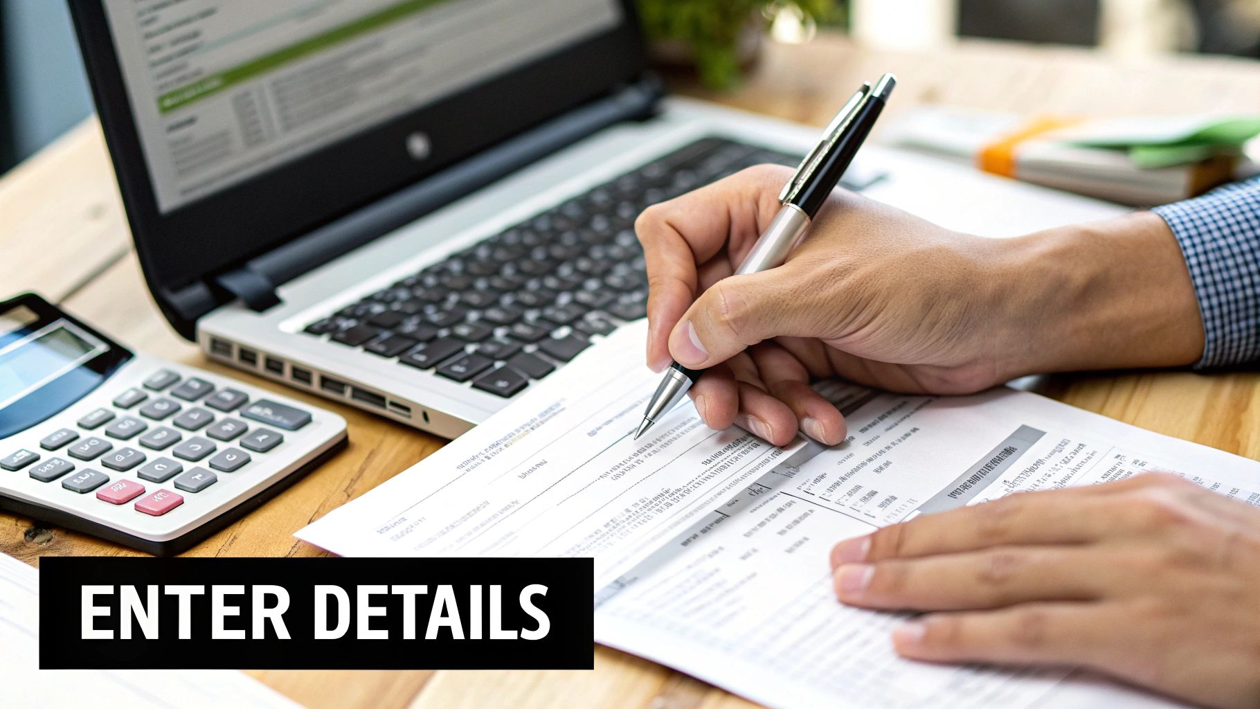 A person's hands writing on a document with a pen, next to a laptop and calculator.