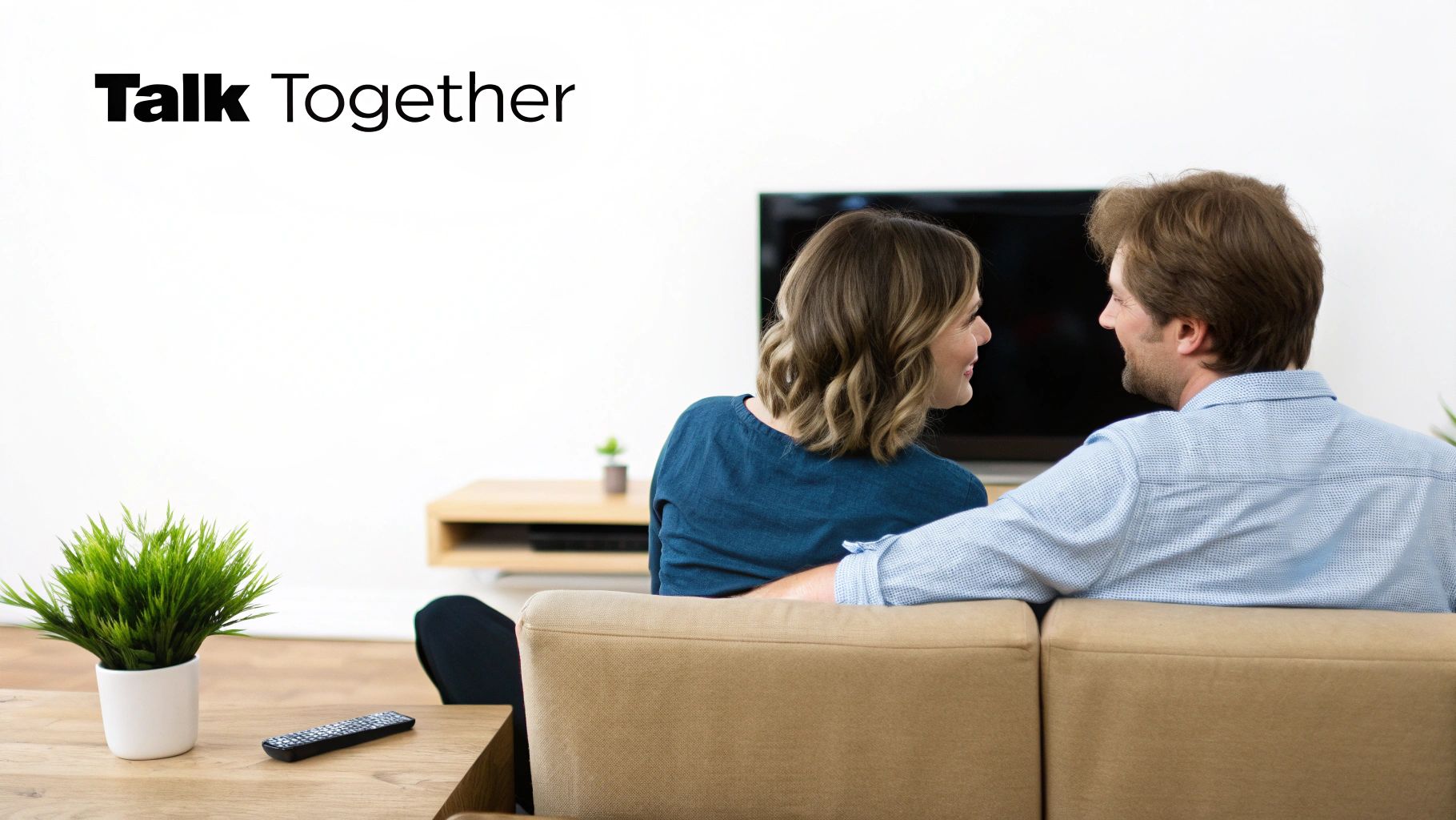 A happy couple sits on a couch, smiling and talking to each other in their living room.