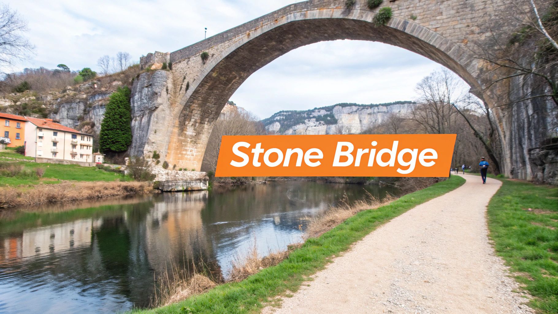 A majestic old stone arch bridge spans a calm river, with houses, cliffs, and a walking path.