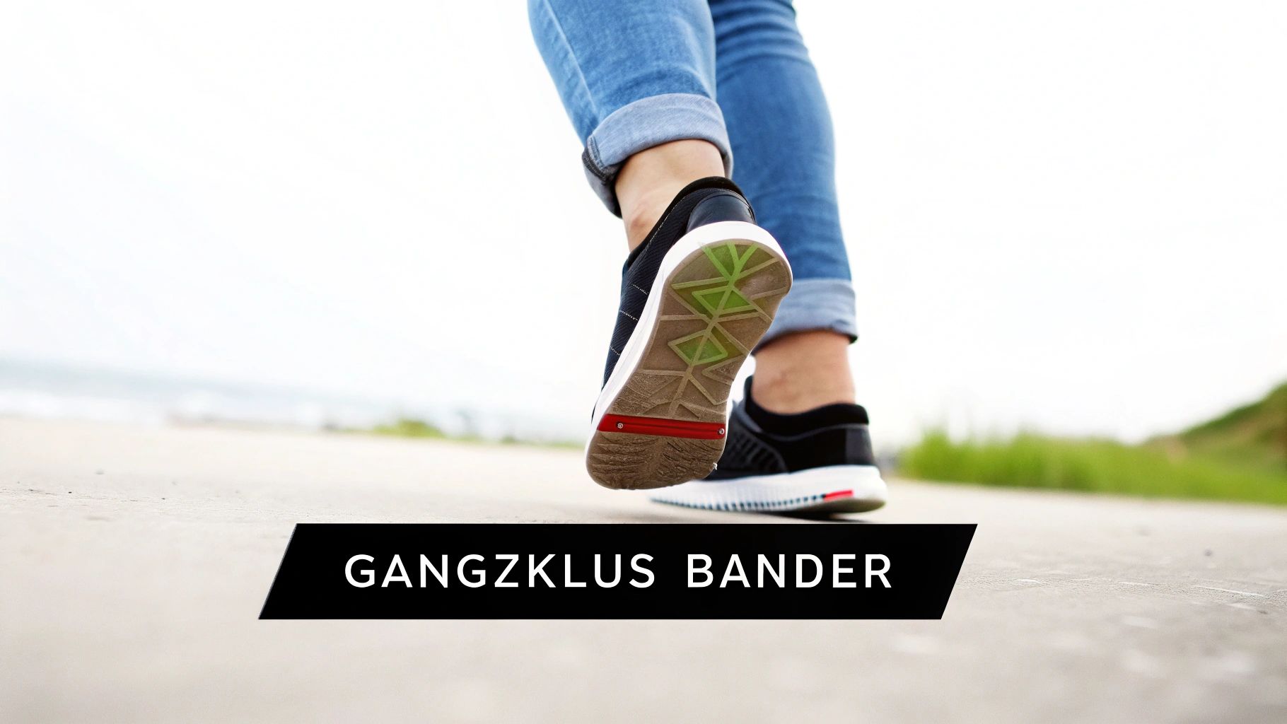 Eine Person in Jeans und schwarzen Turnschuhen geht auf einem Weg. Die Sohle des Schuhs zeigt grüne und rote Details.