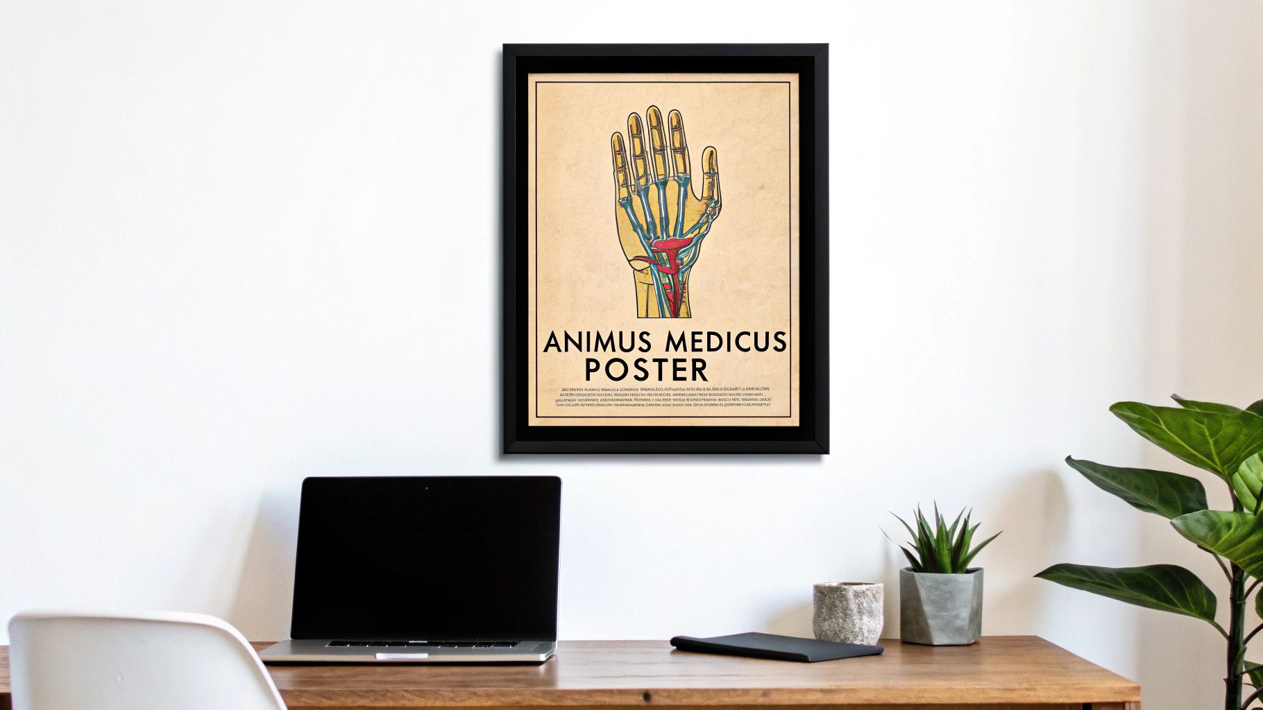 Ein gerahmtes Poster an einer weißen Wand zeigt die Anatomie einer Hand, über einem Schreibtisch mit Laptop und Pflanzen.