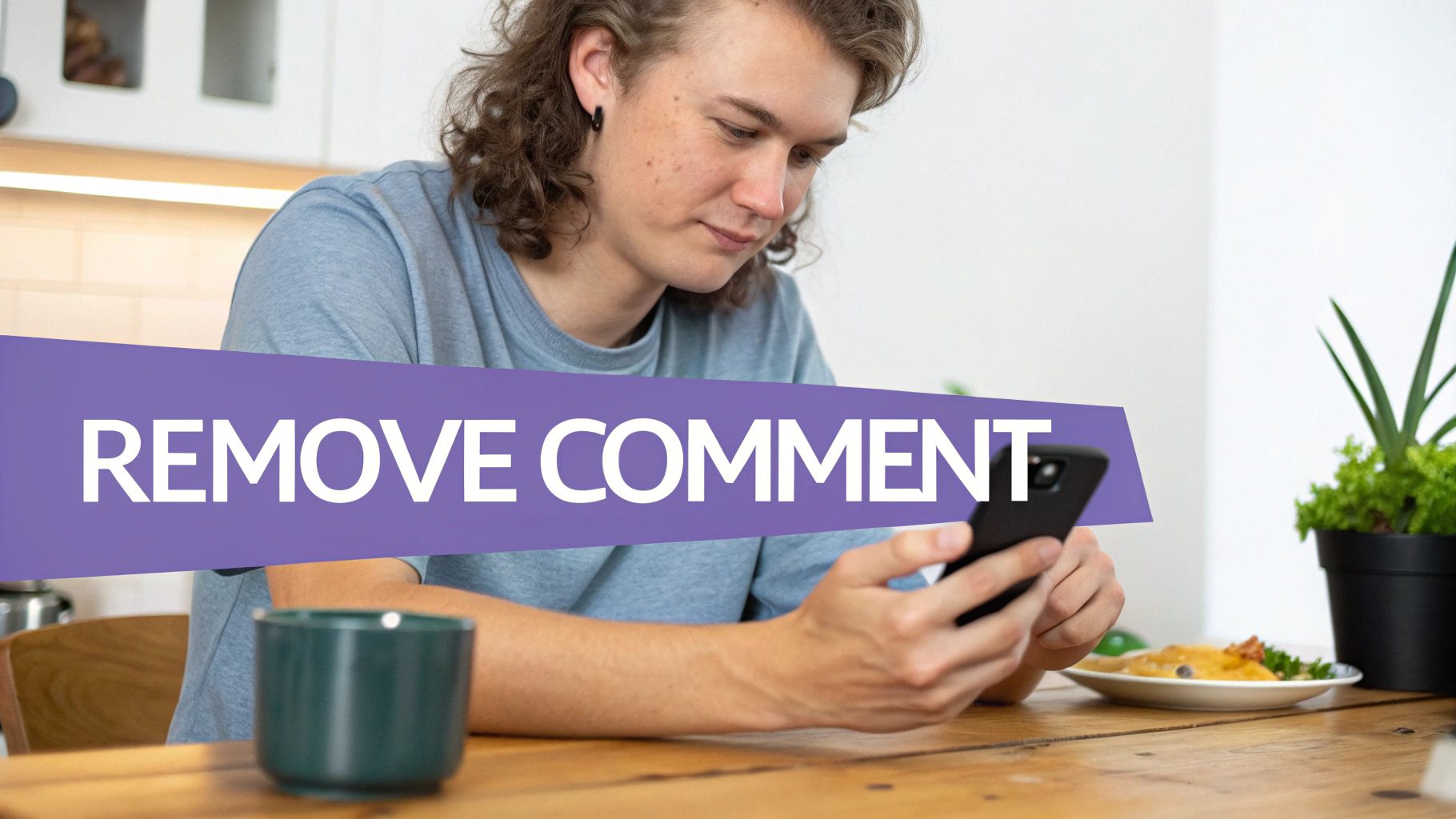 A young man with wavy hair sits at a wooden table, looking at his smartphone.