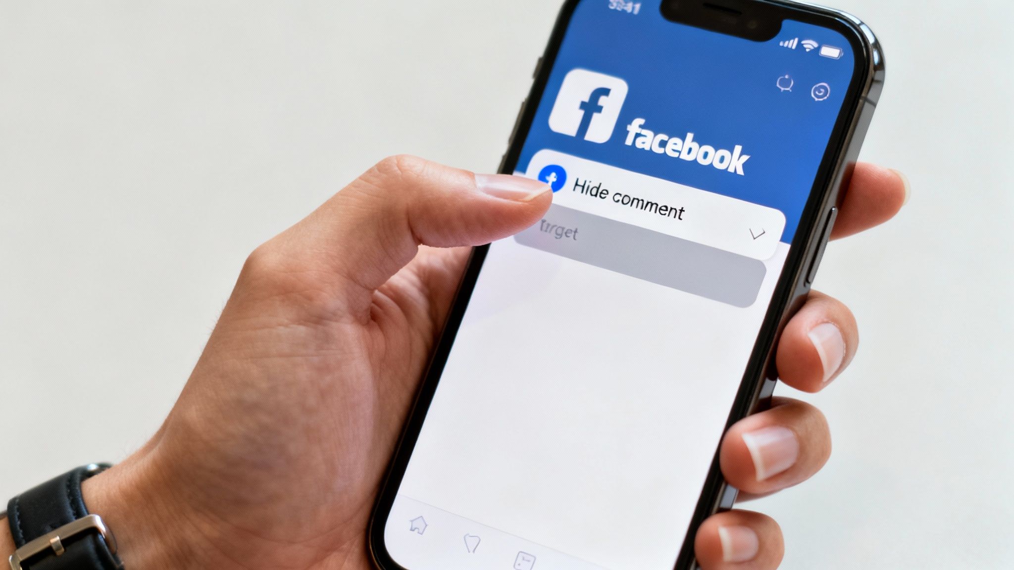 Hand selecting hide comment option on Facebook mobile app displayed on iPhone screen