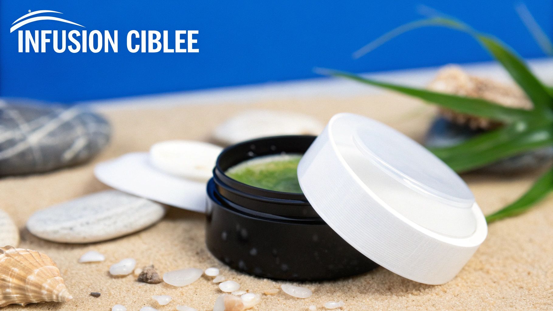 Pot de crème verte, probablement pour les yeux, et son couvercle blanc sur le sable, entouré de coquillages.