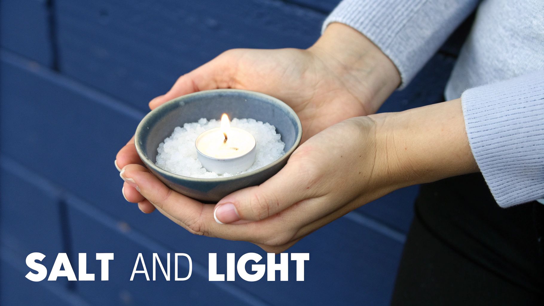 Close-up of hands holding a blue bowl filled with white salt and a small lit candle.