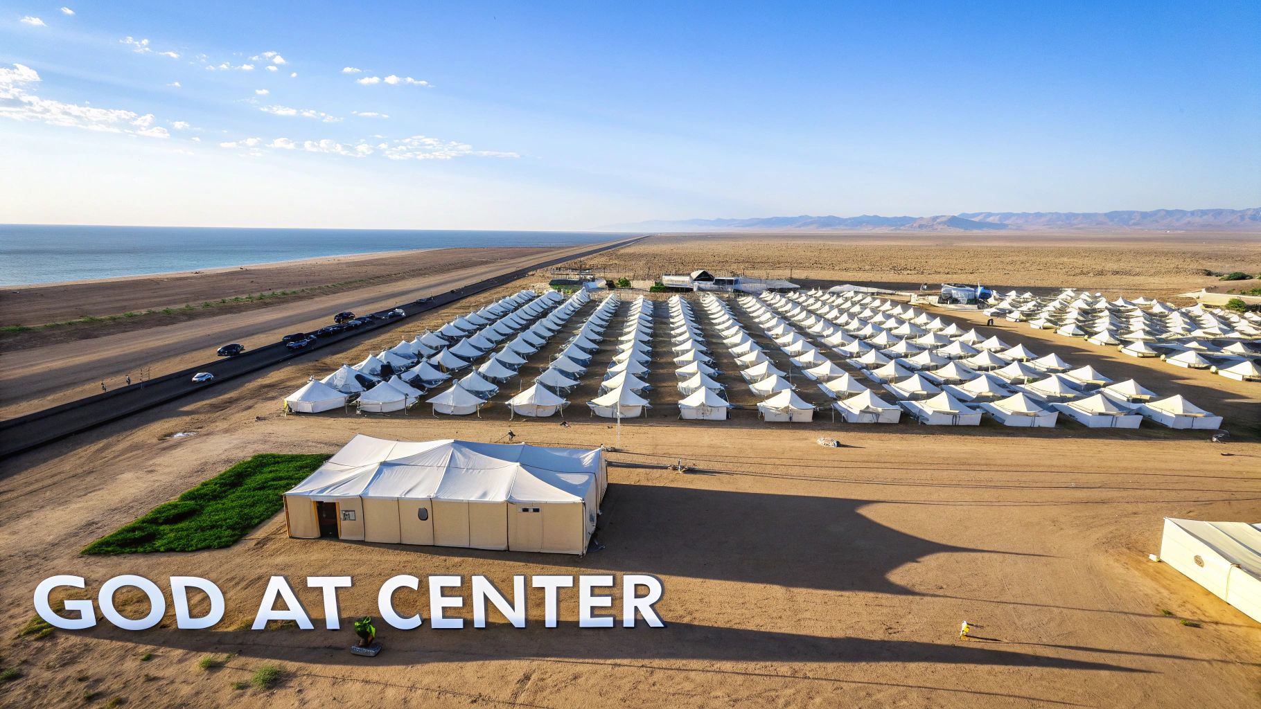 Aerial view of a vast tent camp by the ocean, with a prominent 'GOD AT CENTER' sign.