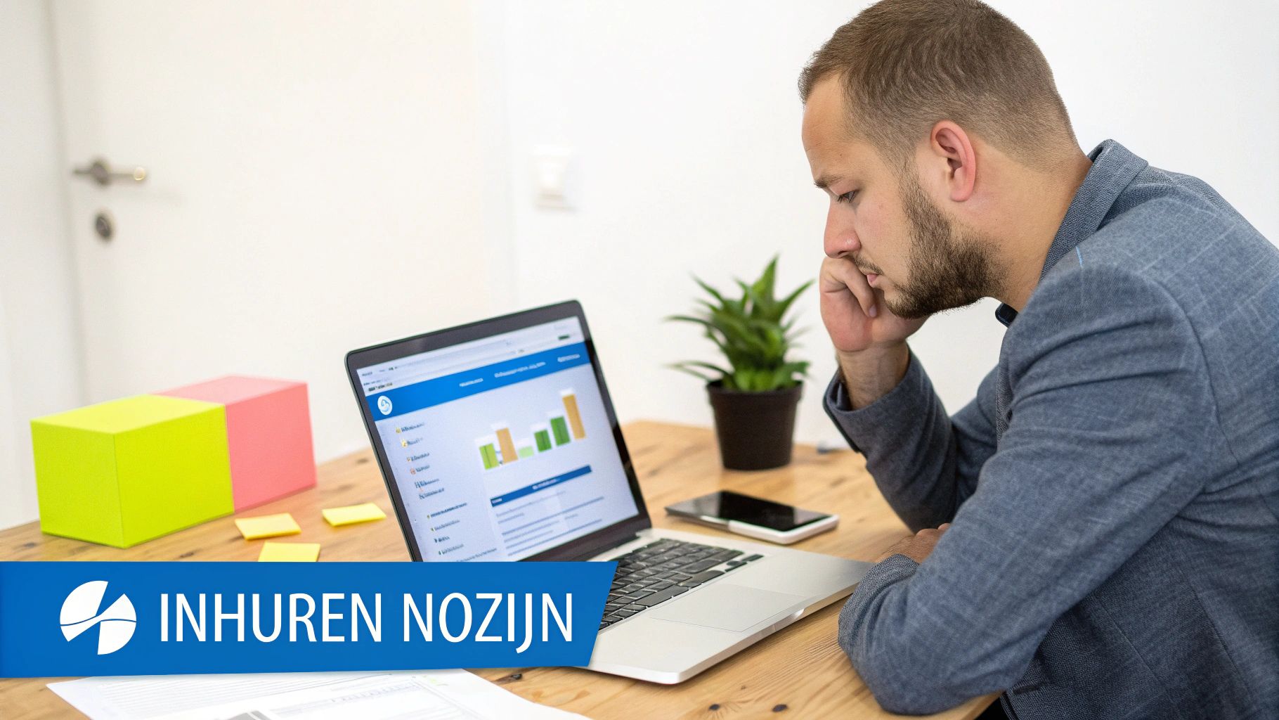 Een man met baard bekijkt geconcentreerd een laptop met grafieken op een houten bureau.