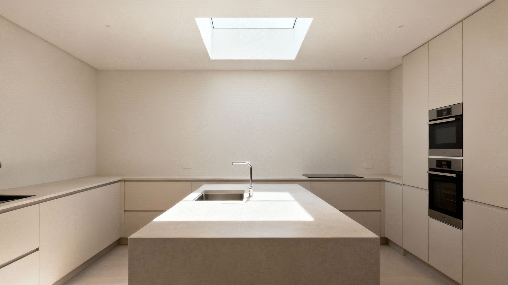 Modern kitchen with minimalist design, central island, built-in ovens, and a bright skylight.