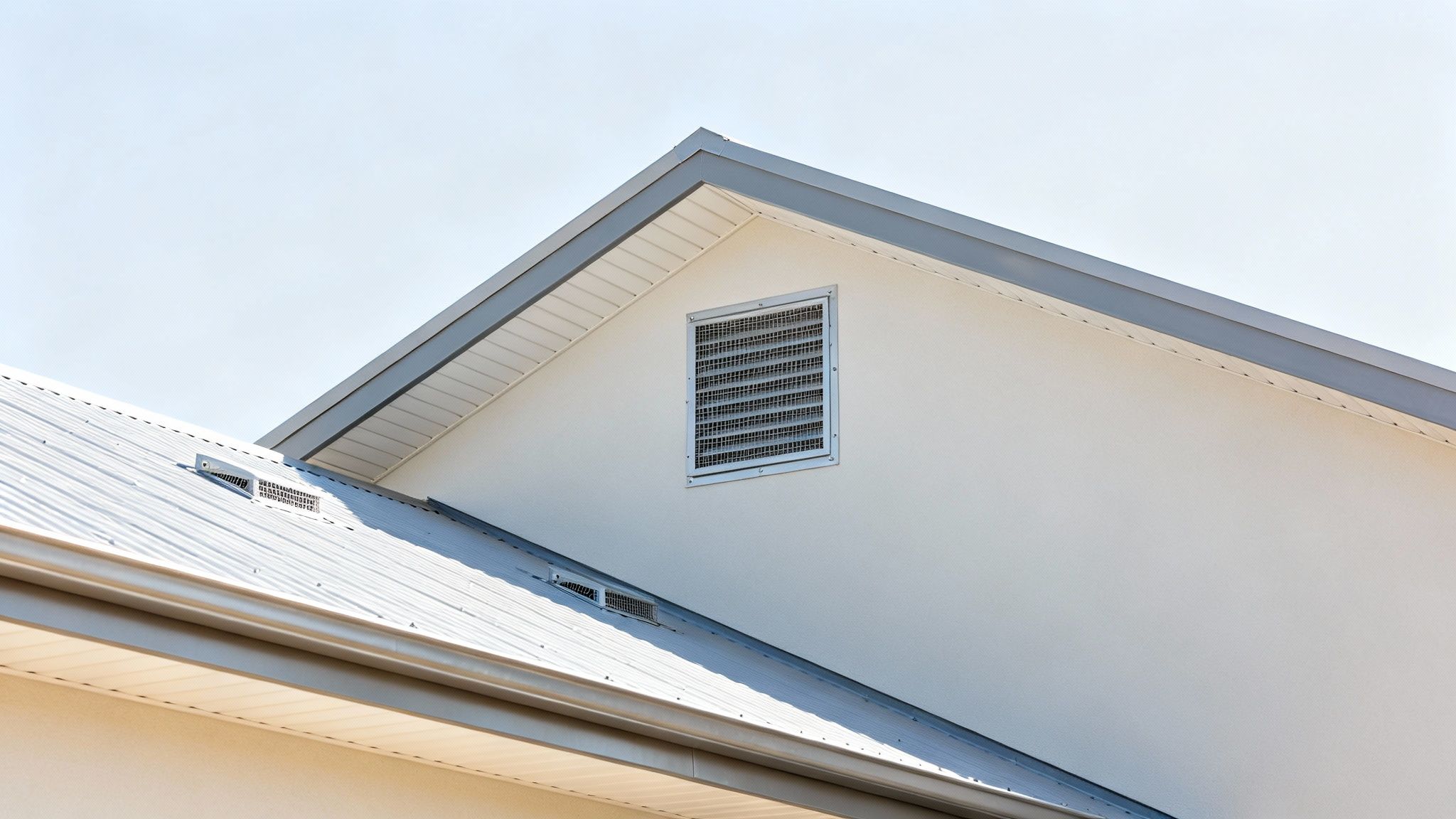 Modern building detail showcasing a gray metal roof, light wall, and a large attic vent.
