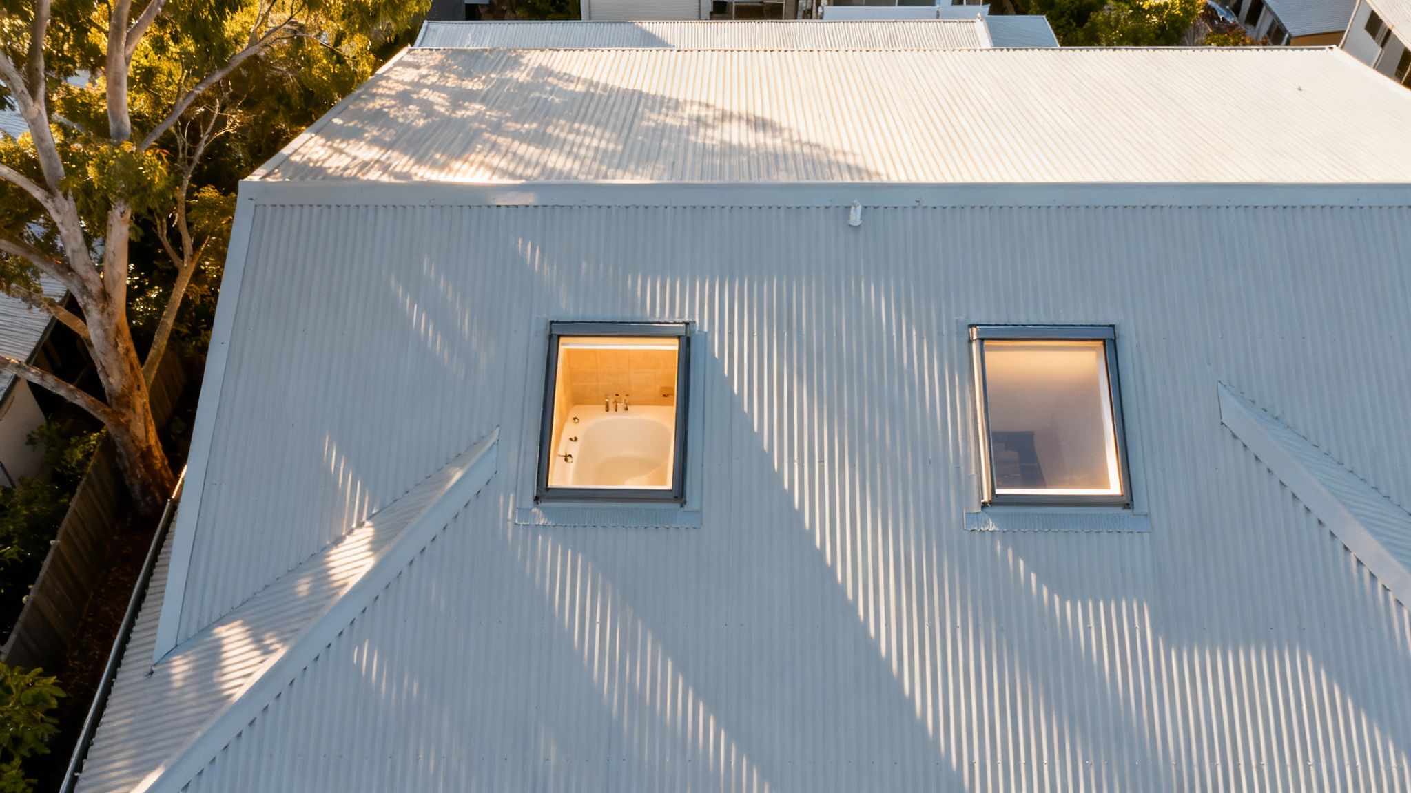 Aerial view of a modern house roof with two skylights, one revealing a bathtub.
