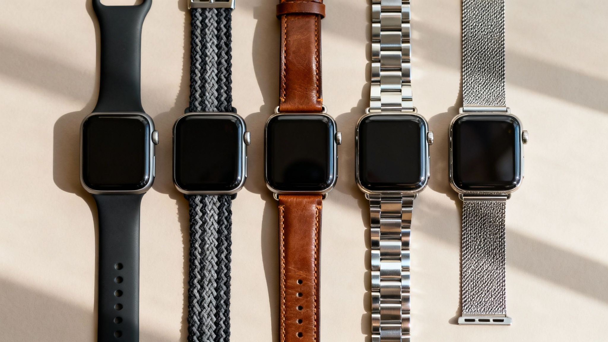 Five Apple Watches displaying various third-party bands: black sport, braided, brown leather, metal link, and Milanese.
