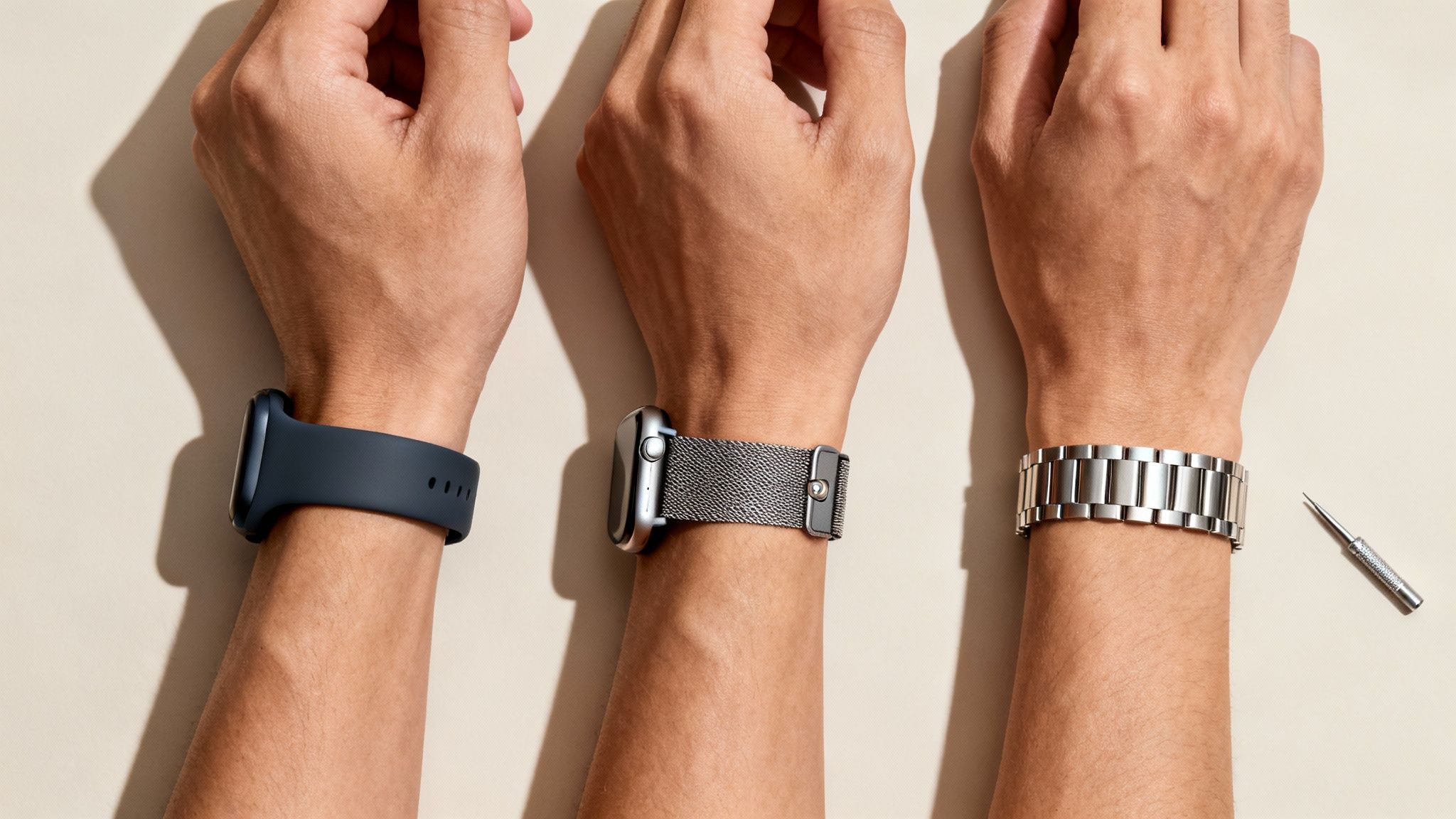 Three wrists display various Apple Watch bands: a dark blue silicone, a silver Milanese loop, and a link bracelet.