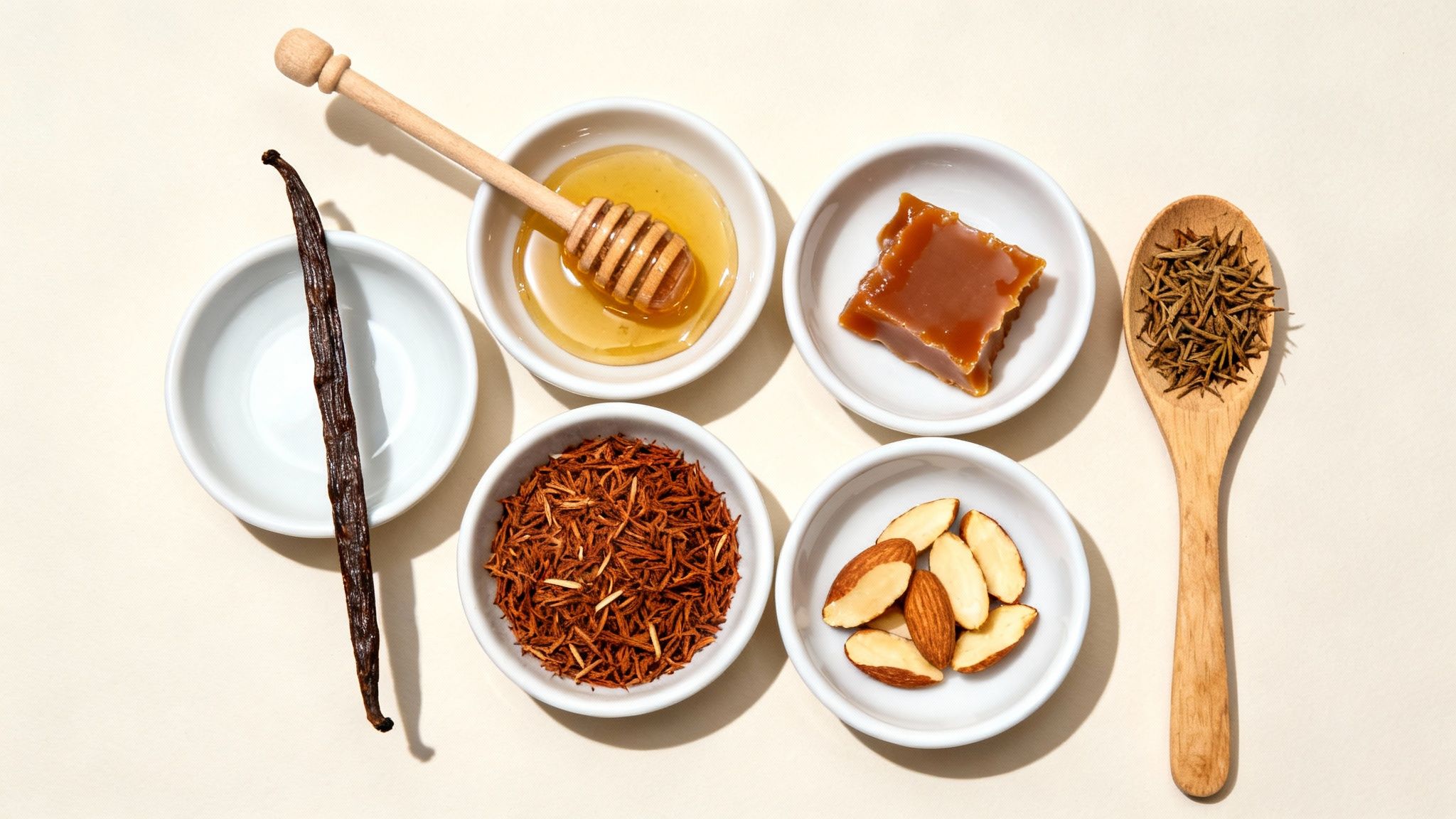 A clear glass teapot filled with brewed rooibos tea, sitting next to a cup and small bowls containing vanilla beans and honey.
