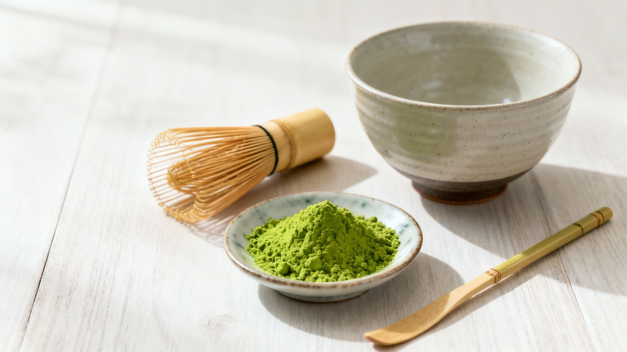 Matcha tea preparation set with whisk, green powder, bowl, and scoop on a wooden surface.