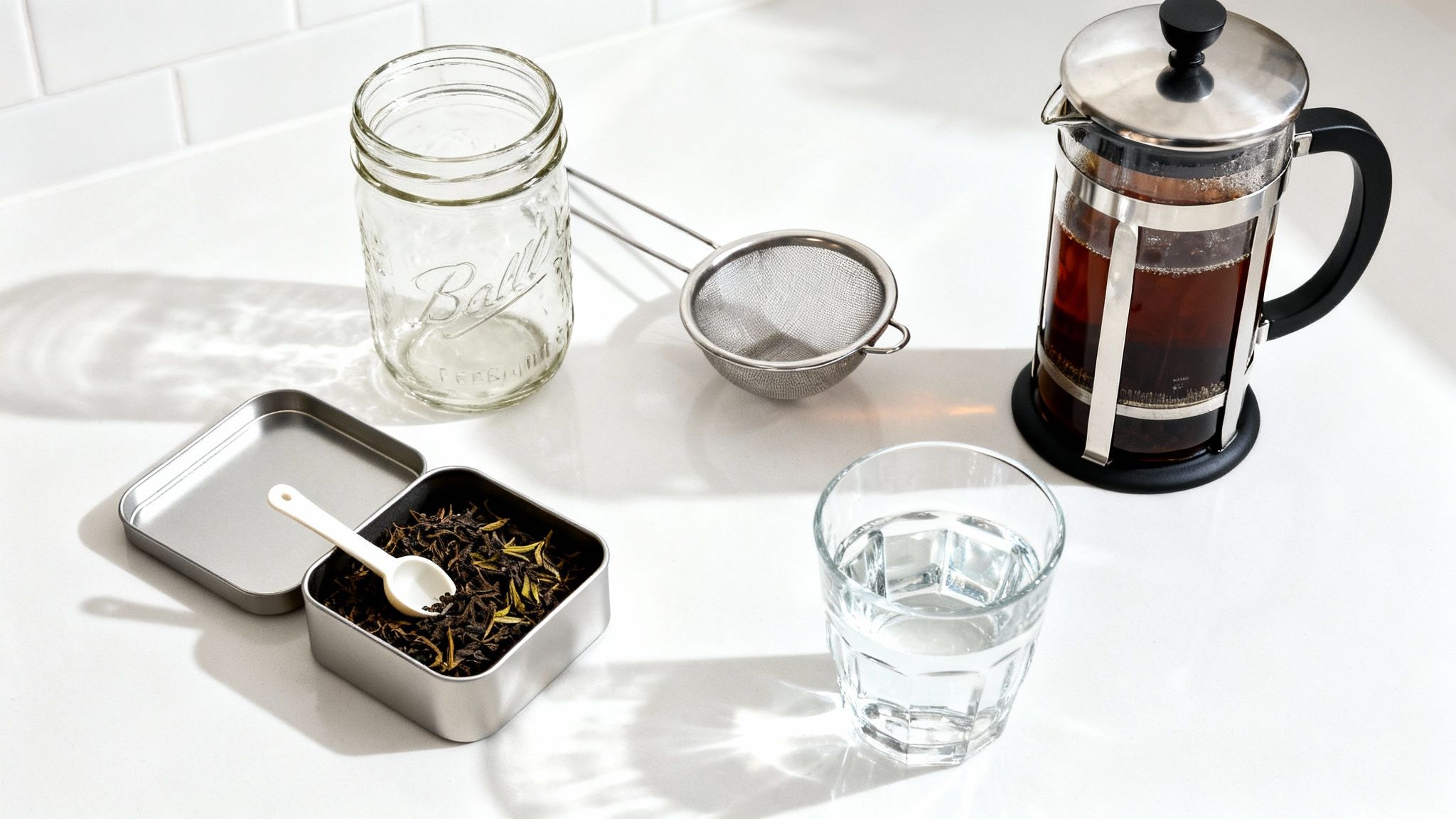 Overhead shot of a french press, loose leaf tea, mason jar, strainer, and water for cold brew tea.