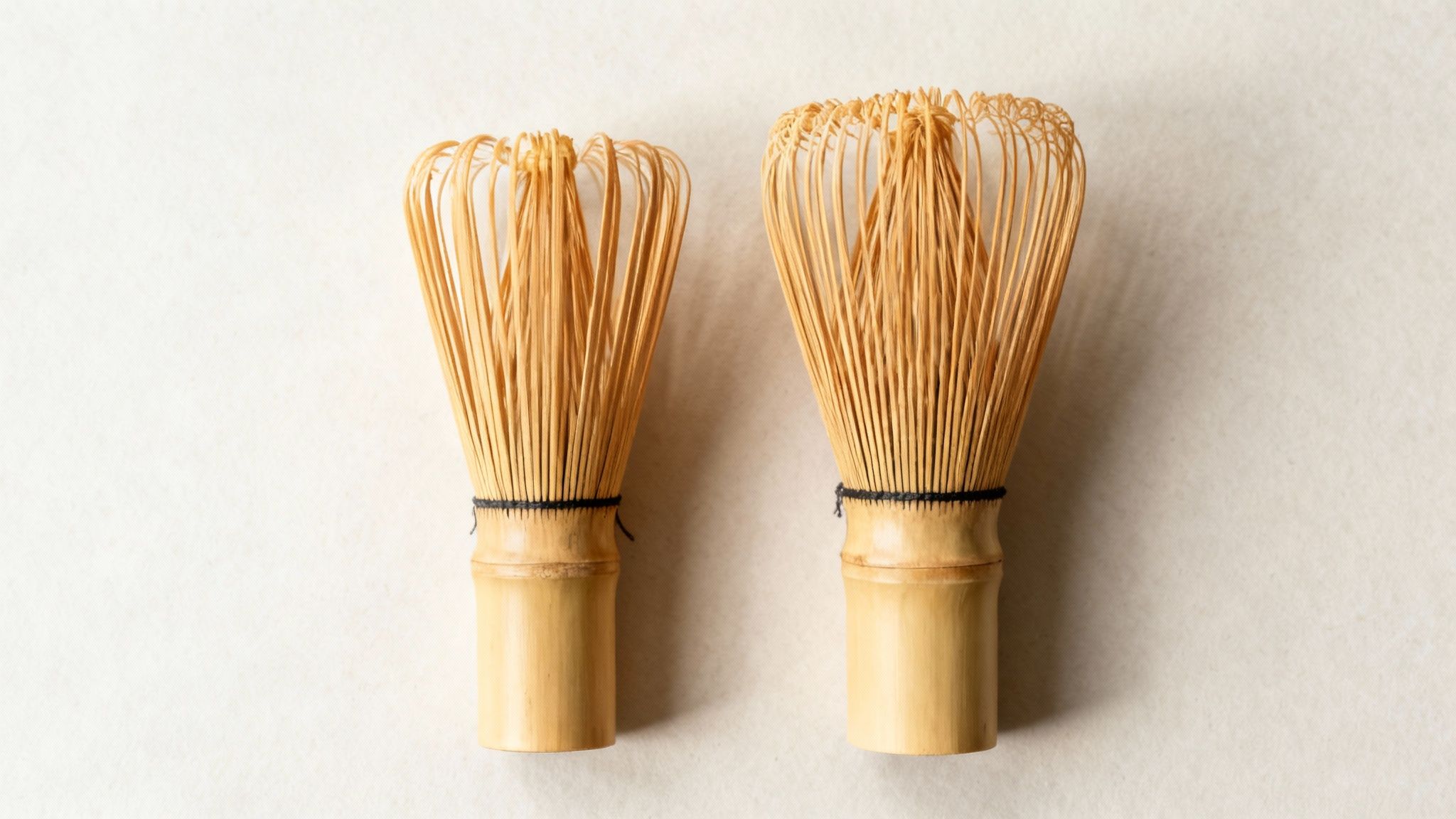 A person holding a matcha green tea bamboo whisk over a traditional matcha bowl