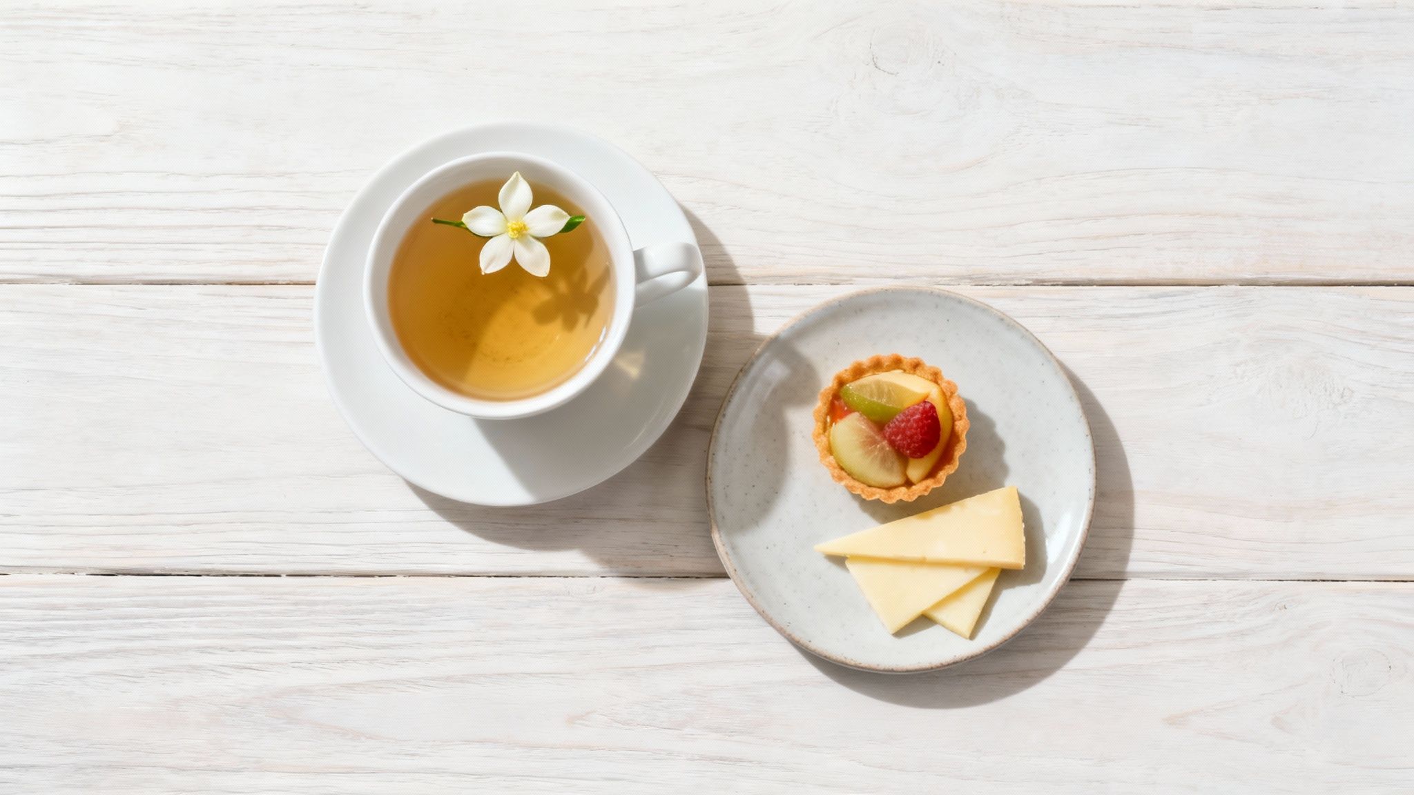 A beautifully arranged platter with fruit tarts, mild cheeses, and a pot of jasmine flowers tea.