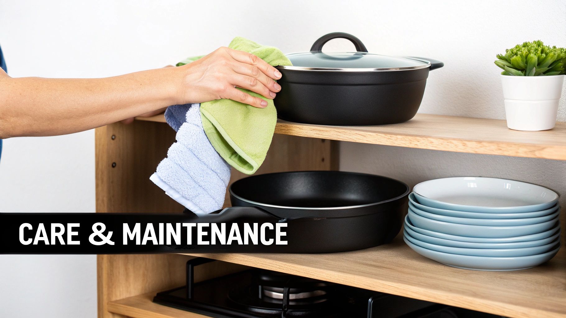A hand cleans a black cooking pot with a green cloth on a wooden shelf. Below are more pans and stacked blue plates.