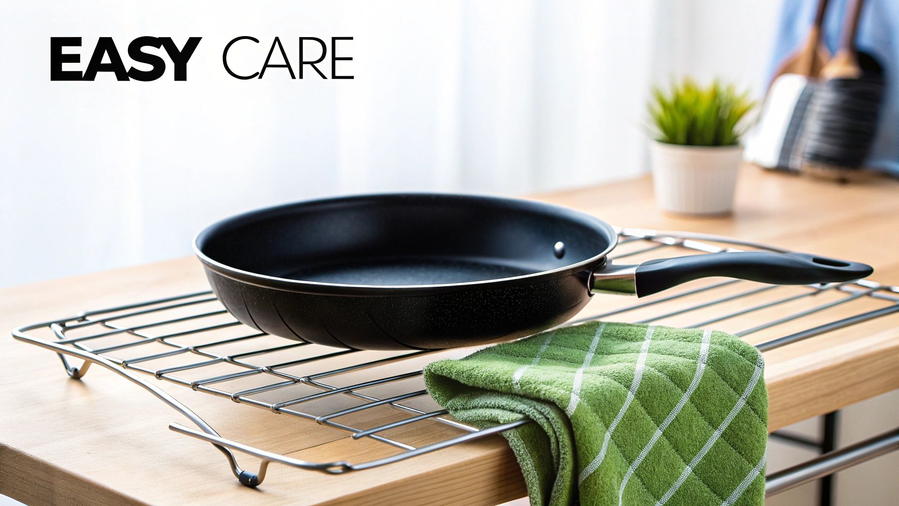 A black frying pan rests on a metal cooling rack next to a green checkered towel on a wooden counter, highlighting 'EASY CARE'.
