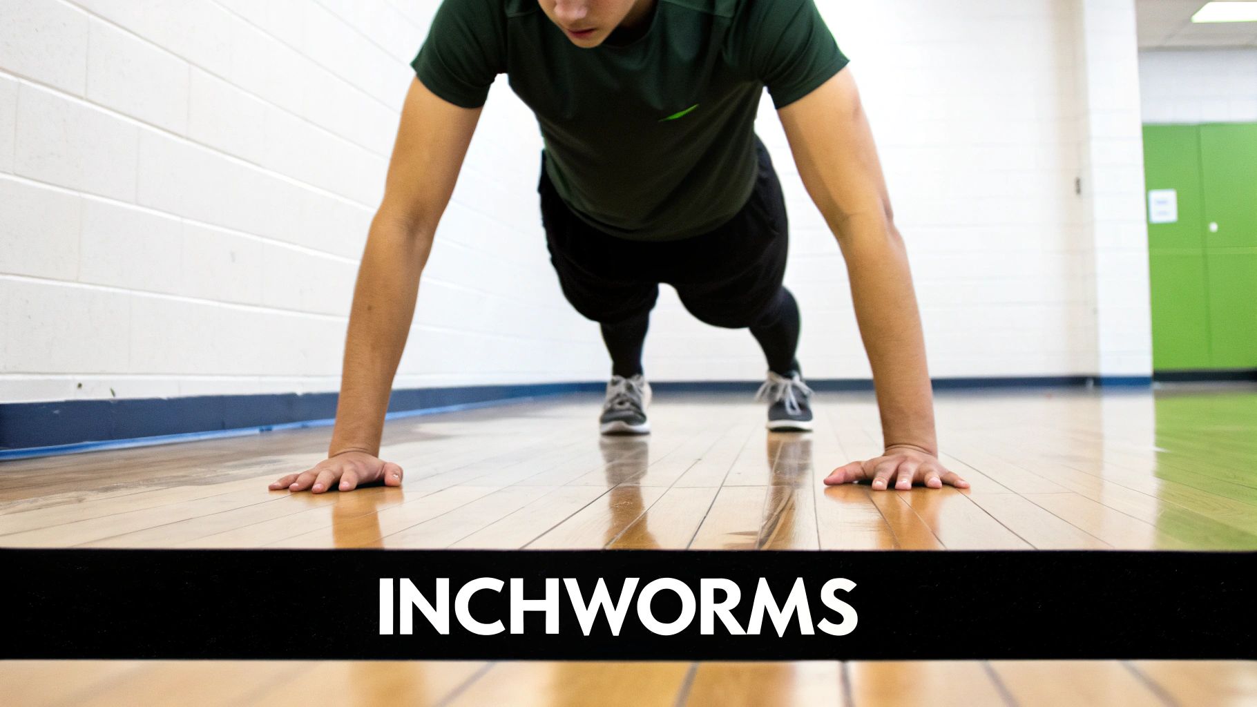 Person performing inchworm exercise on gym floor, hands planted with body in plank position