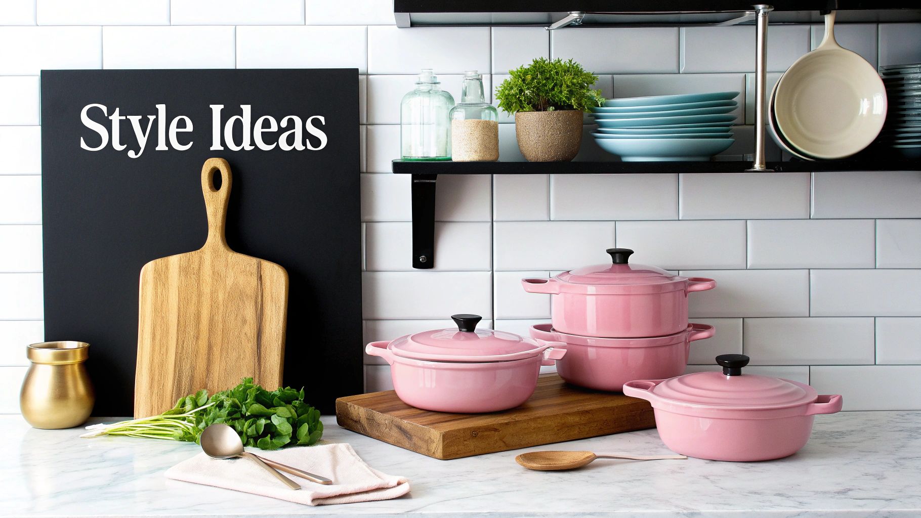 A stylish kitchen counter features pink cookware, a wooden cutting board, and fresh greens on a marble surface.