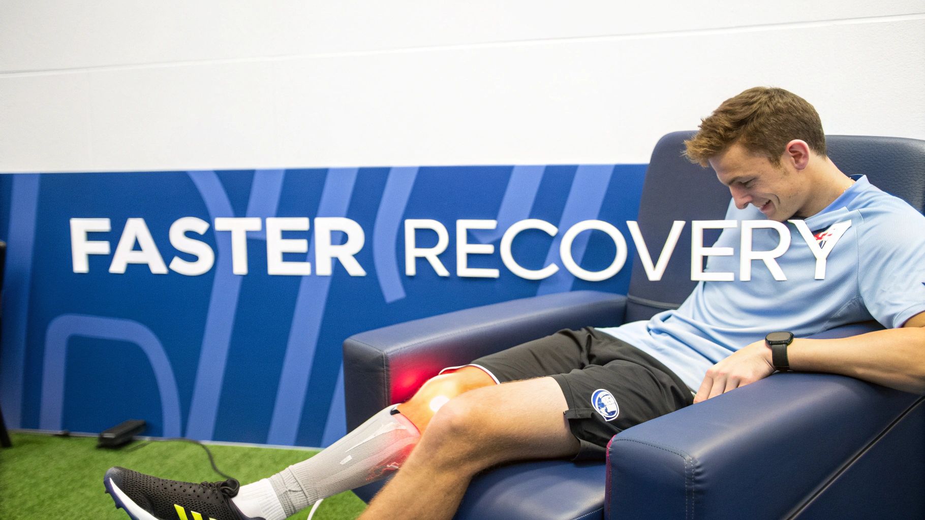 A smiling man sits in a chair, receiving infrared light therapy on his knee for recovery.