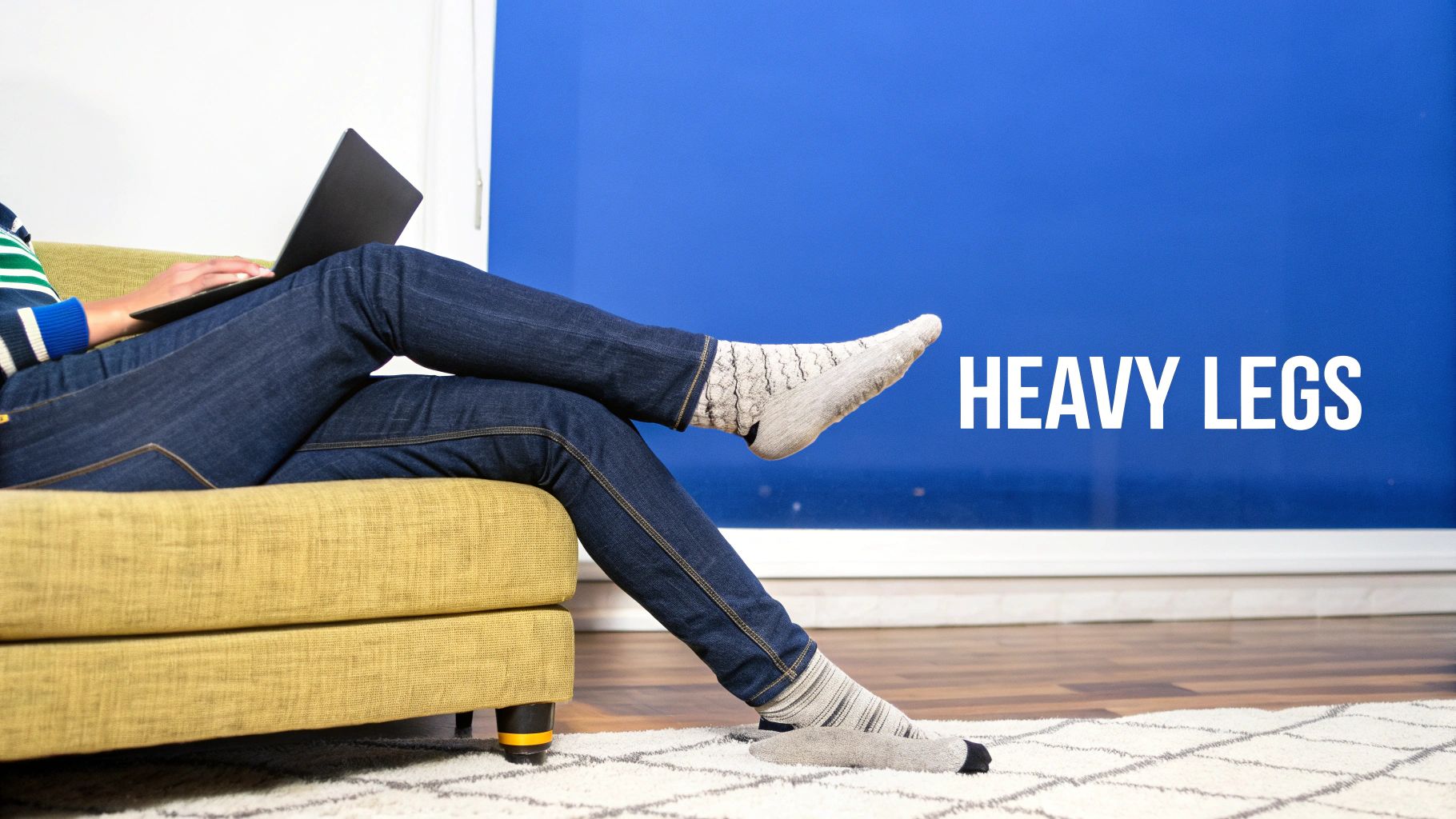 A person sitting on a couch with a laptop, one sock removed, illustrating heavy legs.