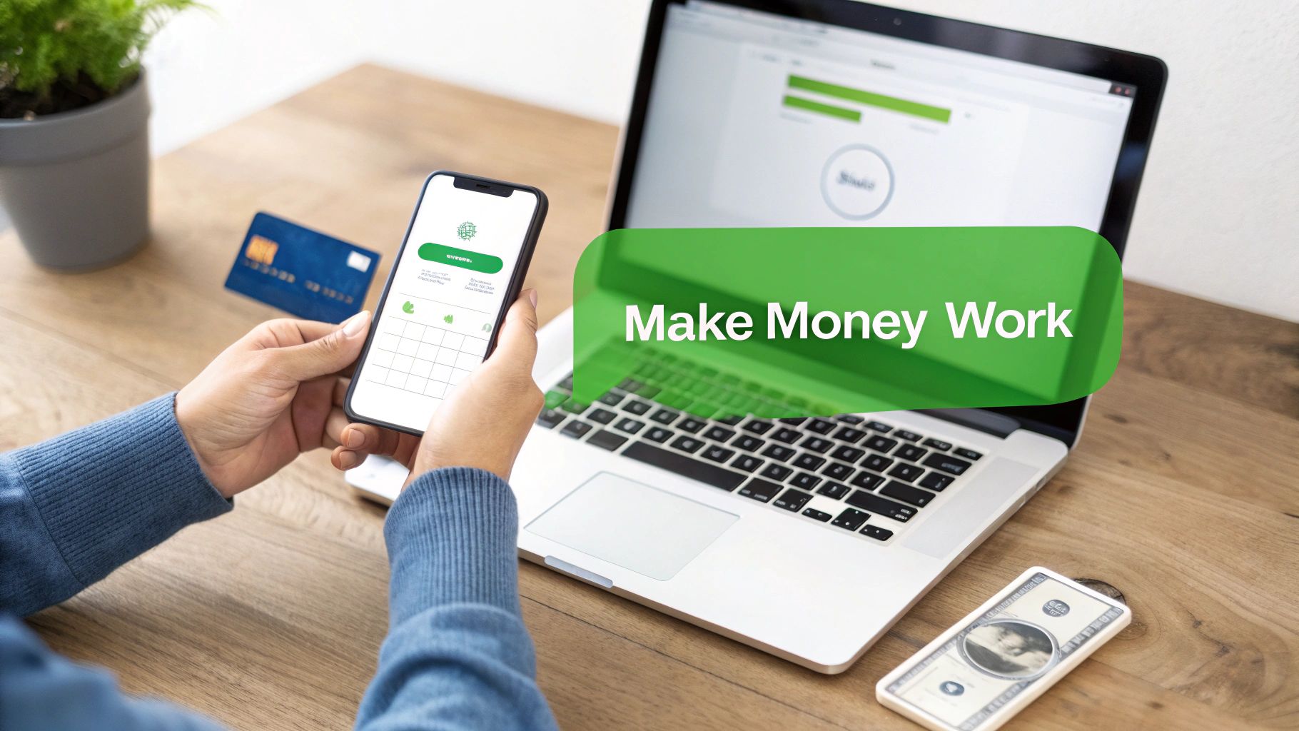 Person using a smartphone and laptop for online banking, with a credit card on a wooden desk.