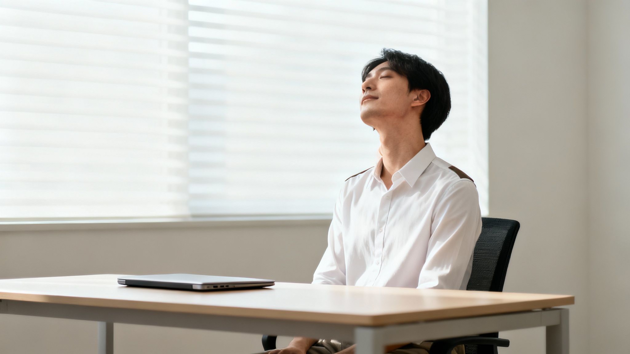 En mand med lukkede øjne strækker sin nakke ved et skrivebord med en bærbar computer.