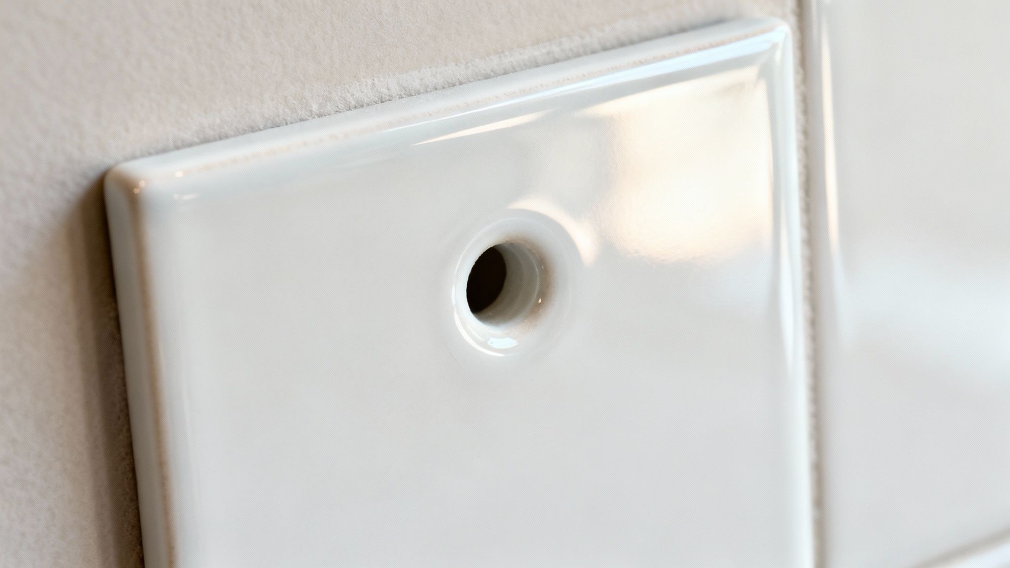 Nærbillede af en hvid keramisk flise med et rent boret hul, klar til installation.