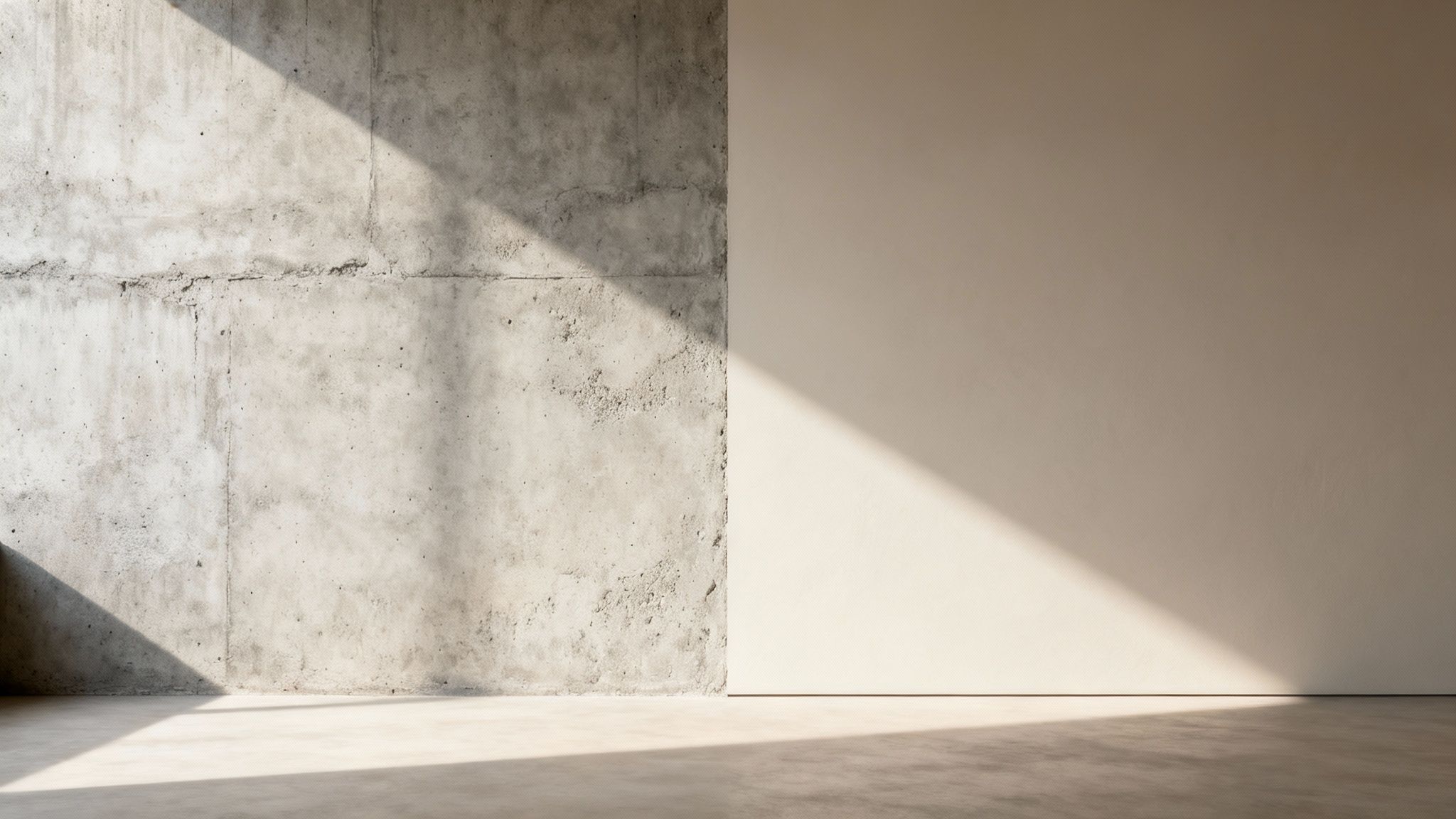 Minimalistisk rum med rå betonvæg, glat lys væg og dramatiske sollysskygger på gulv og vægge.