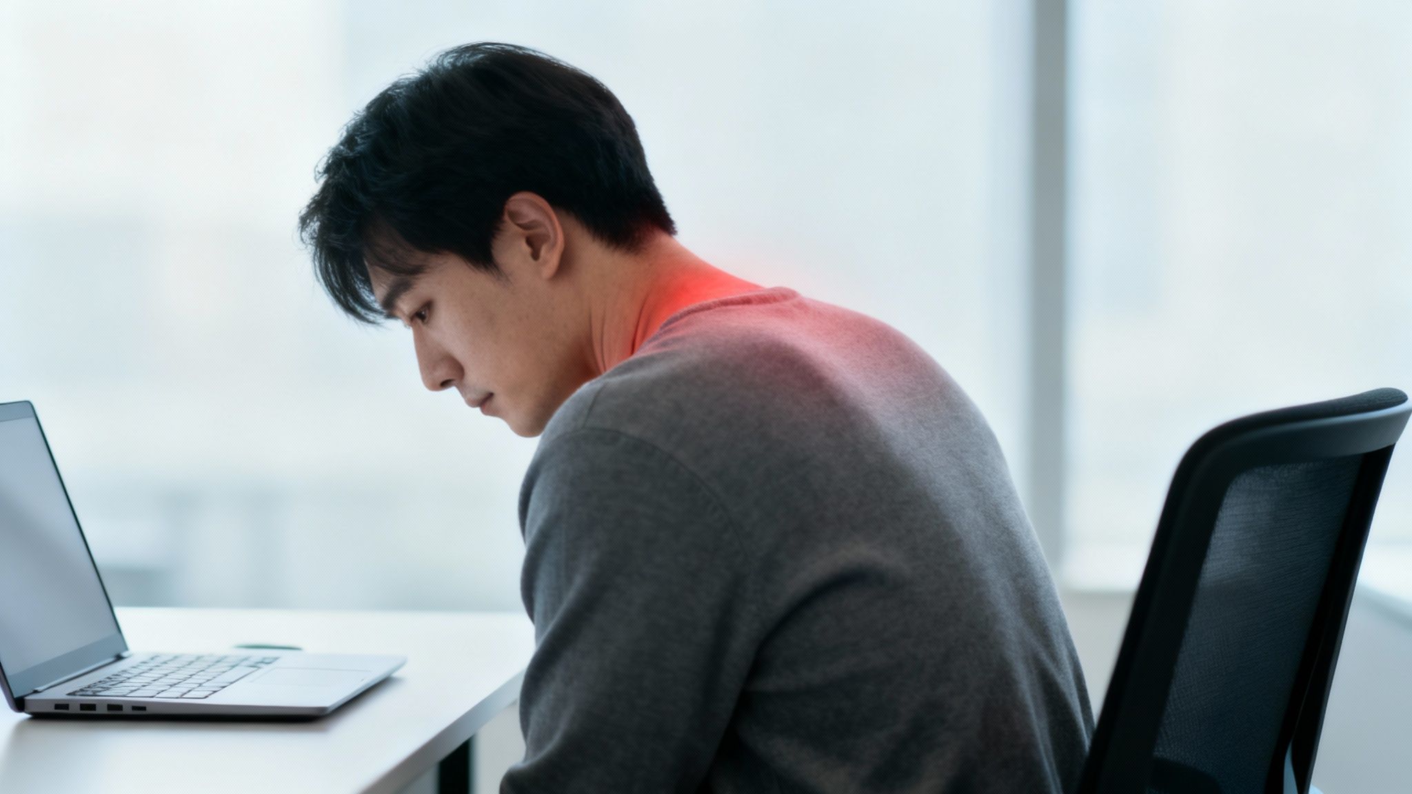 En ung mand med smerter i nakke og skuldre, mens han arbejder ved en bærbar computer.
