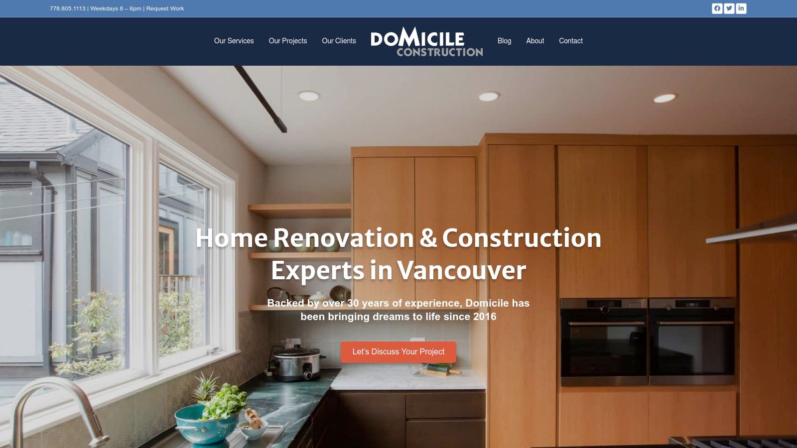 A modern kitchen renovation by Domicile Construction Inc. showing white cabinetry, a large island with a dark countertop, and stainless steel appliances.