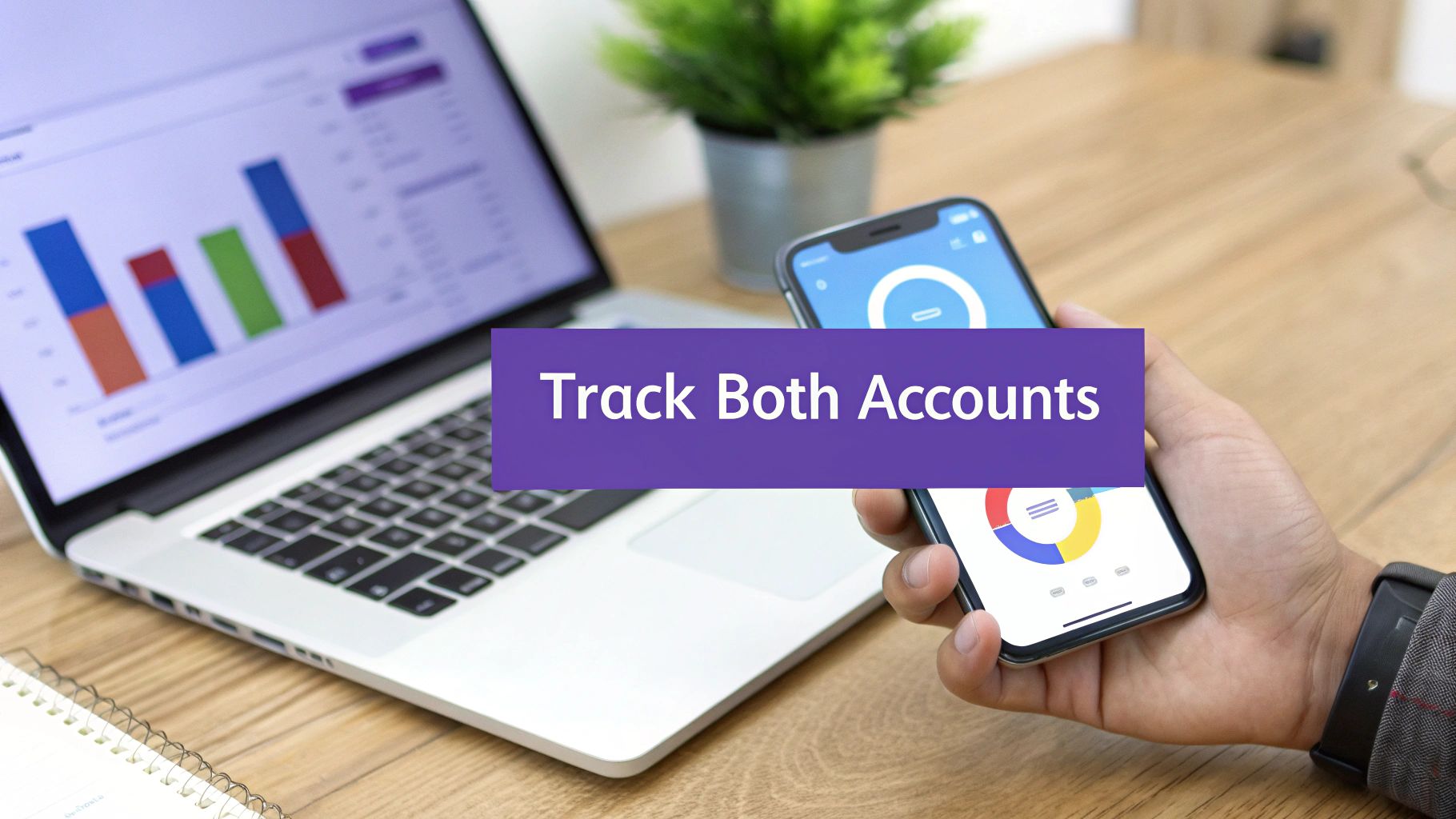 A person's hand holds a smartphone next to a laptop displaying financial data and charts.