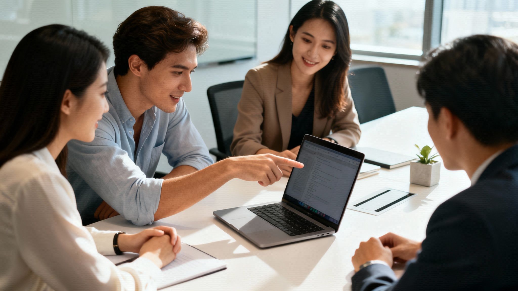 A team of young professionals collaborating, with one man pointing at a laptop screen in an office.