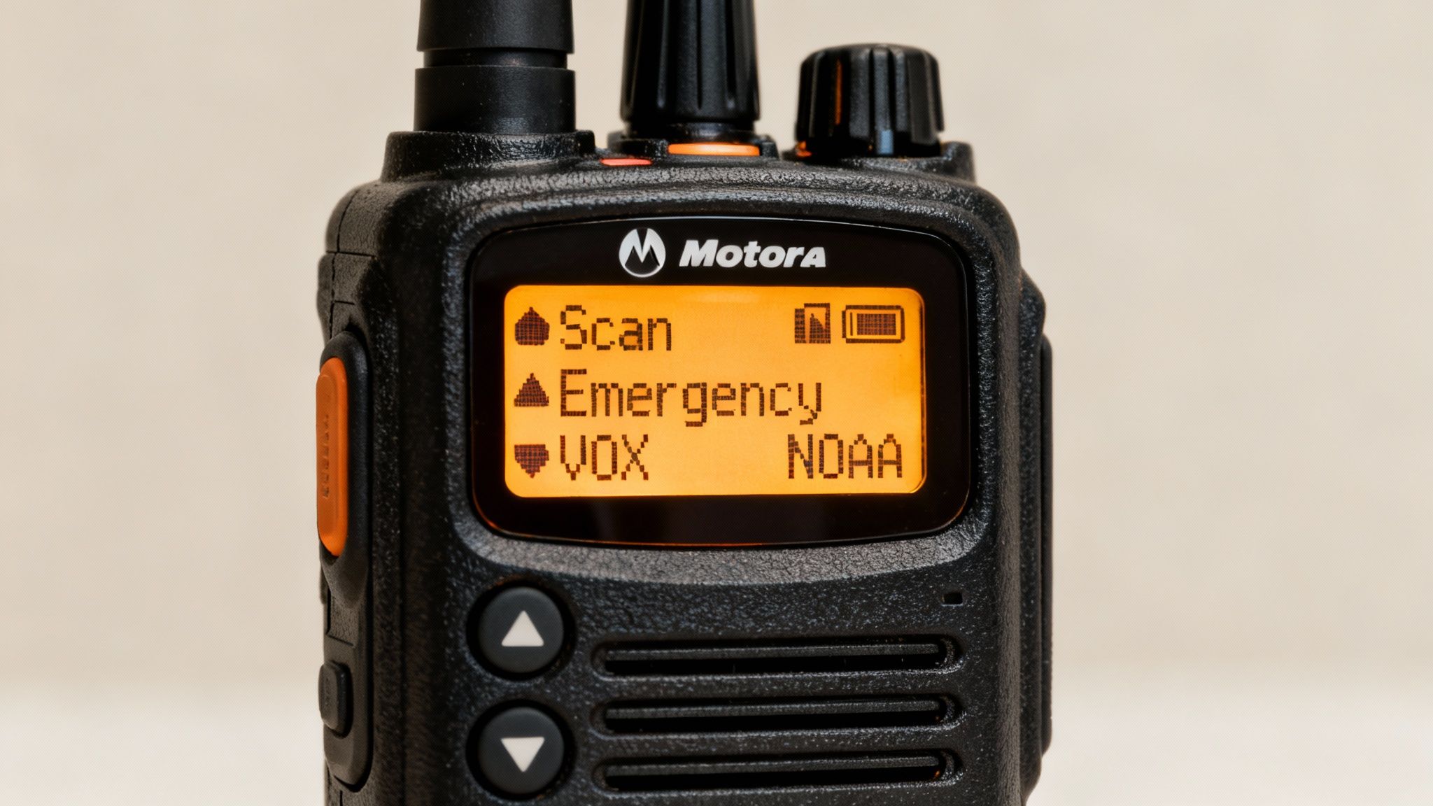A close-up of a black Motorola walkie-talkie with an orange screen displaying menu options like Scan and Emergency.