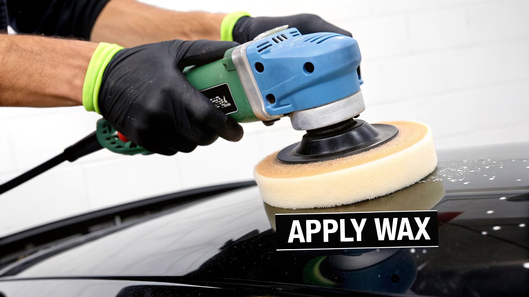 A person in black gloves uses a polishing machine to apply wax to a black car surface.