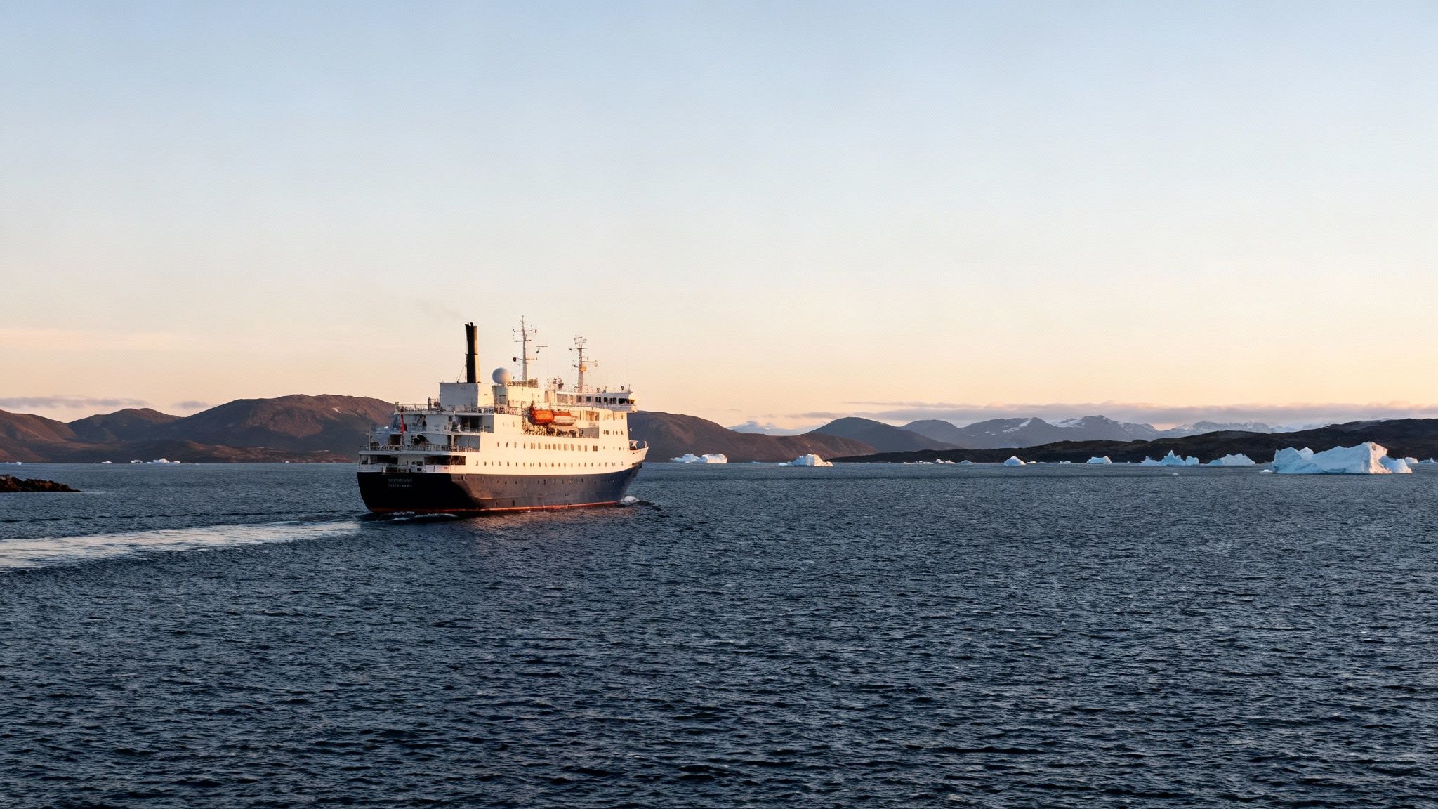 Ship sails across dark blue water, mountains in background, icebergs scattered in the distance.