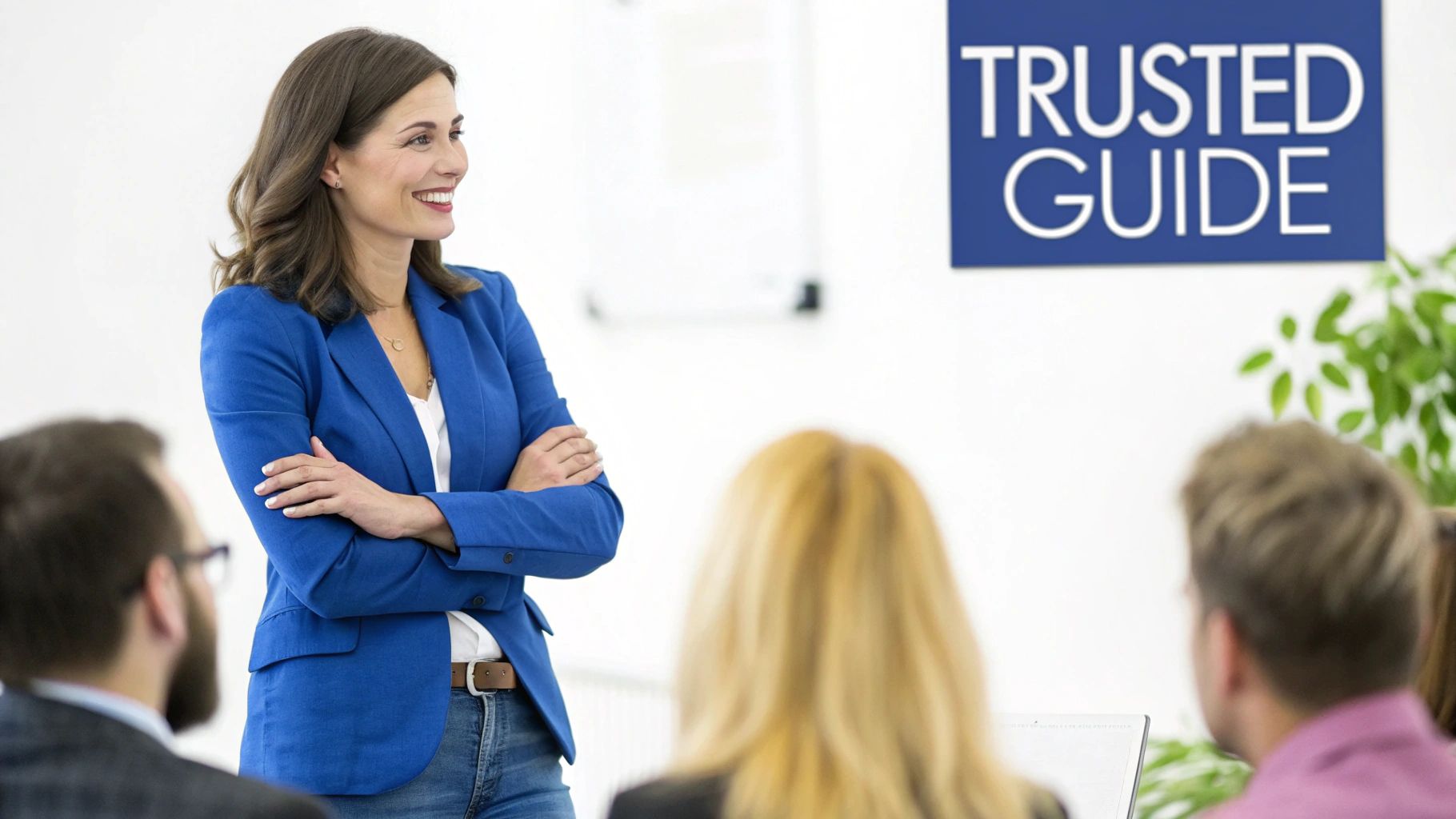 A smiling female speaker in a blue blazer presents to an audience under a 'TRUSTED GUIDE' sign.