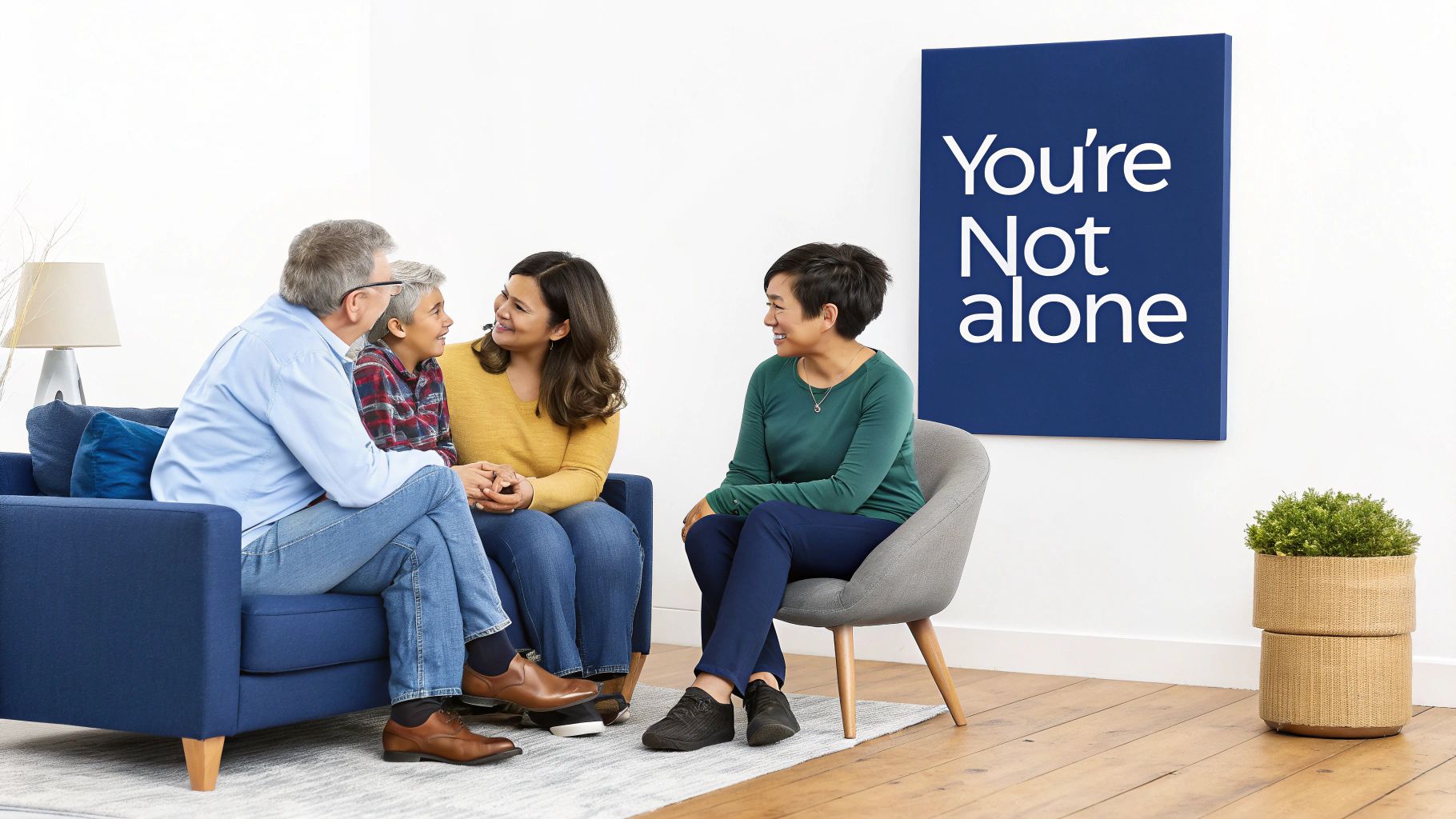Four diverse individuals, including adults and a child, smiling and conversing in a bright room with a "You're Not alone" sign.