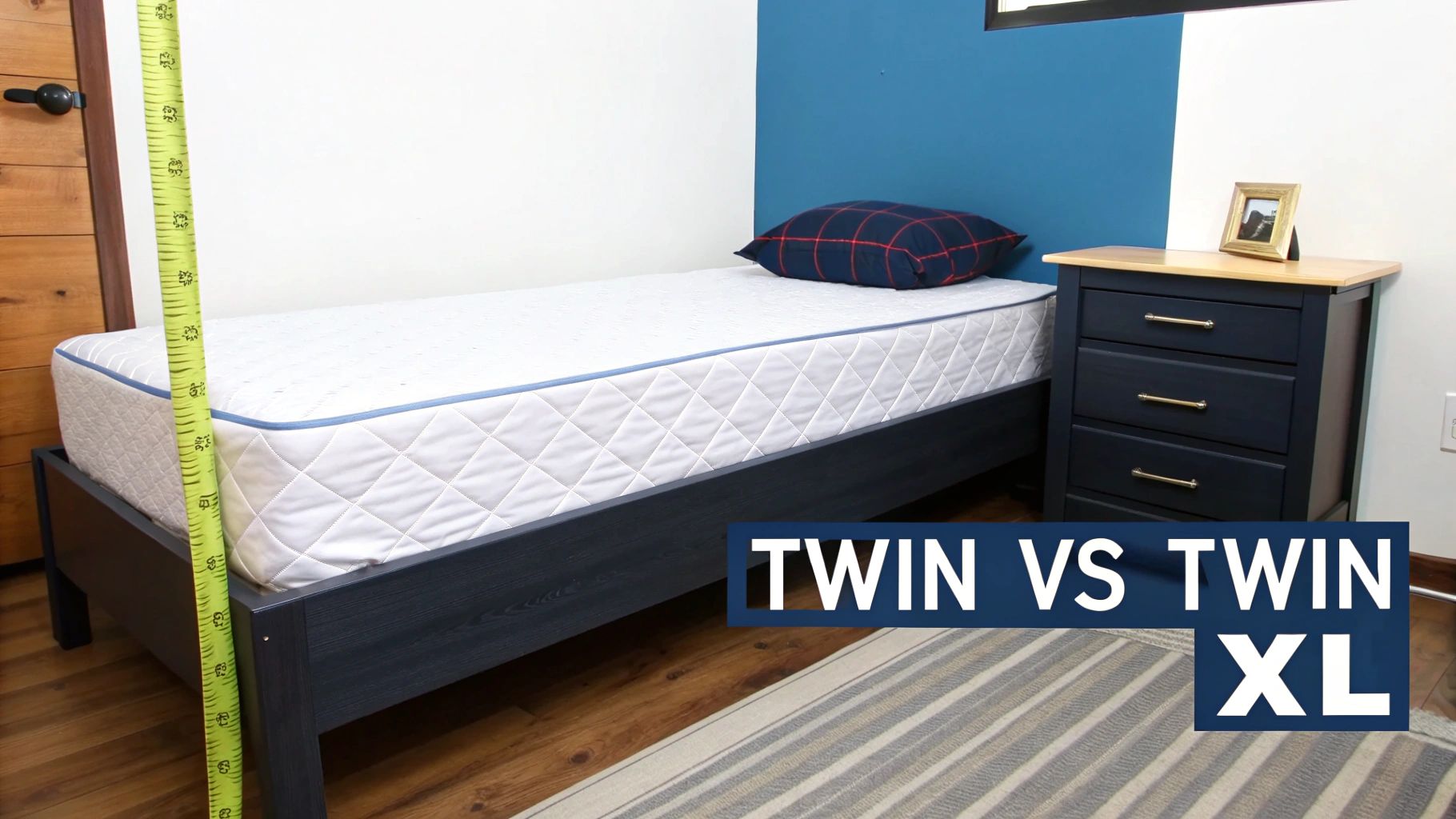 A twin bed with a white mattress and dark blue frame. A ruler measures its length for size comparison.