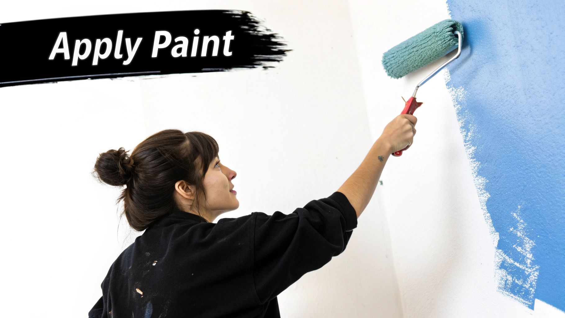 A painter using a roller to apply fresh white paint to a wall, showing proper technique.