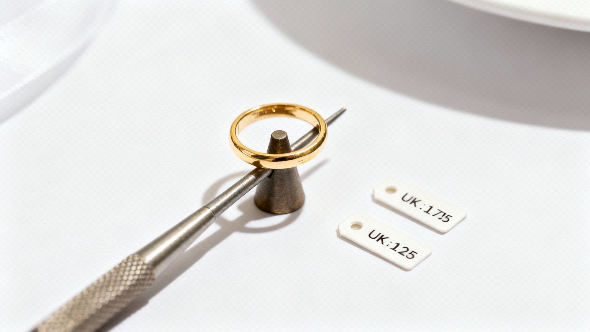 A professional jeweller carefully measuring a gold ring with a sizing tool in a well-lit workshop.
