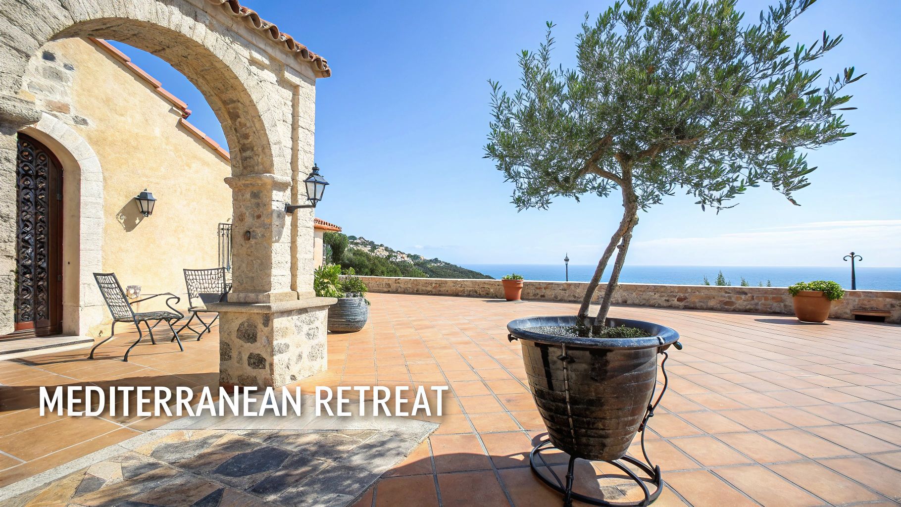 A beautiful Mediterranean patio with a stone archway, olive tree, outdoor furniture, and a stunning sea view.